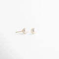Aretes dorados con perla blanca redonda, acabado pulido y diseño refinado que destaca por su brillo natural y sutileza.