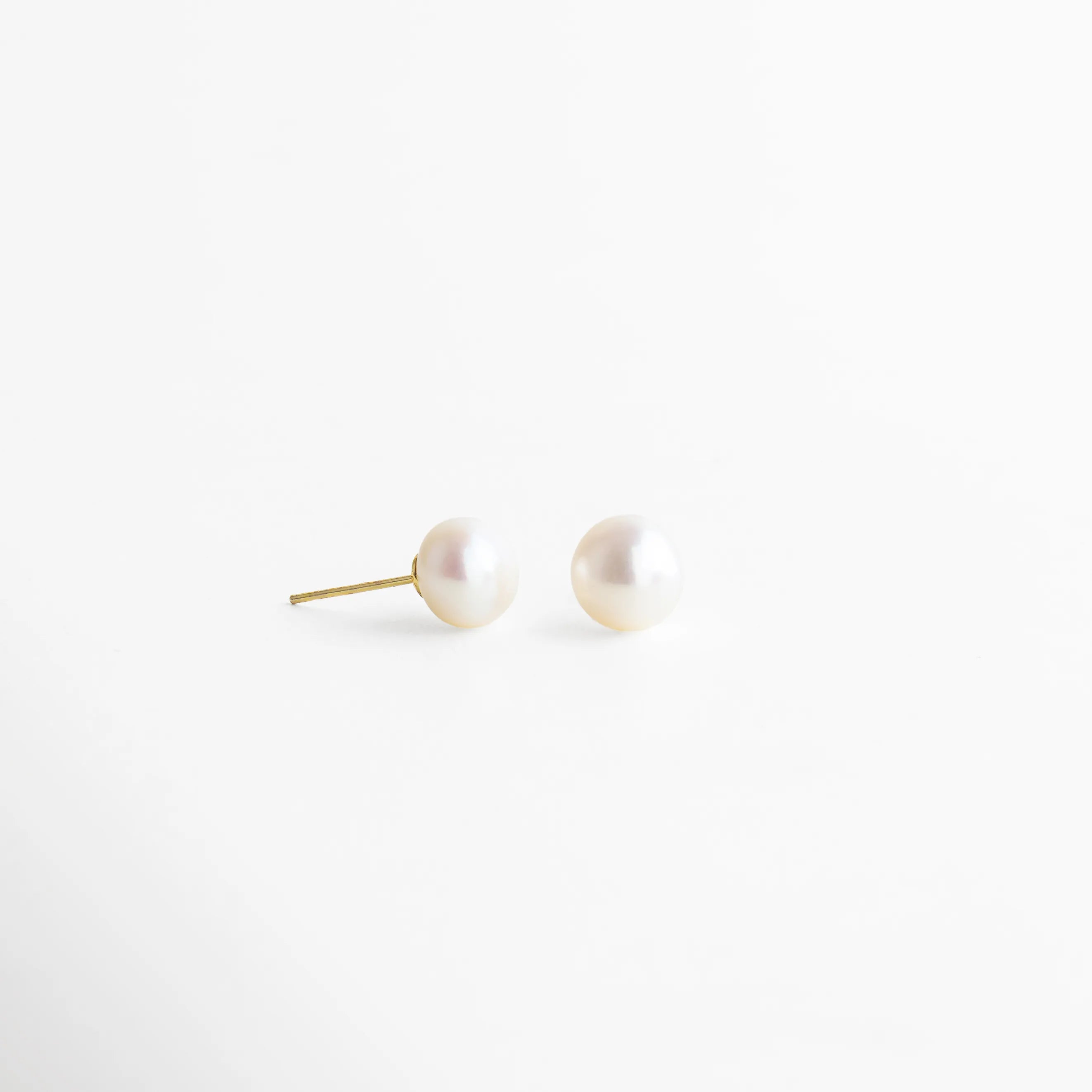 Aretes dorados con perla blanca redonda, acabado pulido y diseño refinado que destaca por su brillo natural y sutileza.