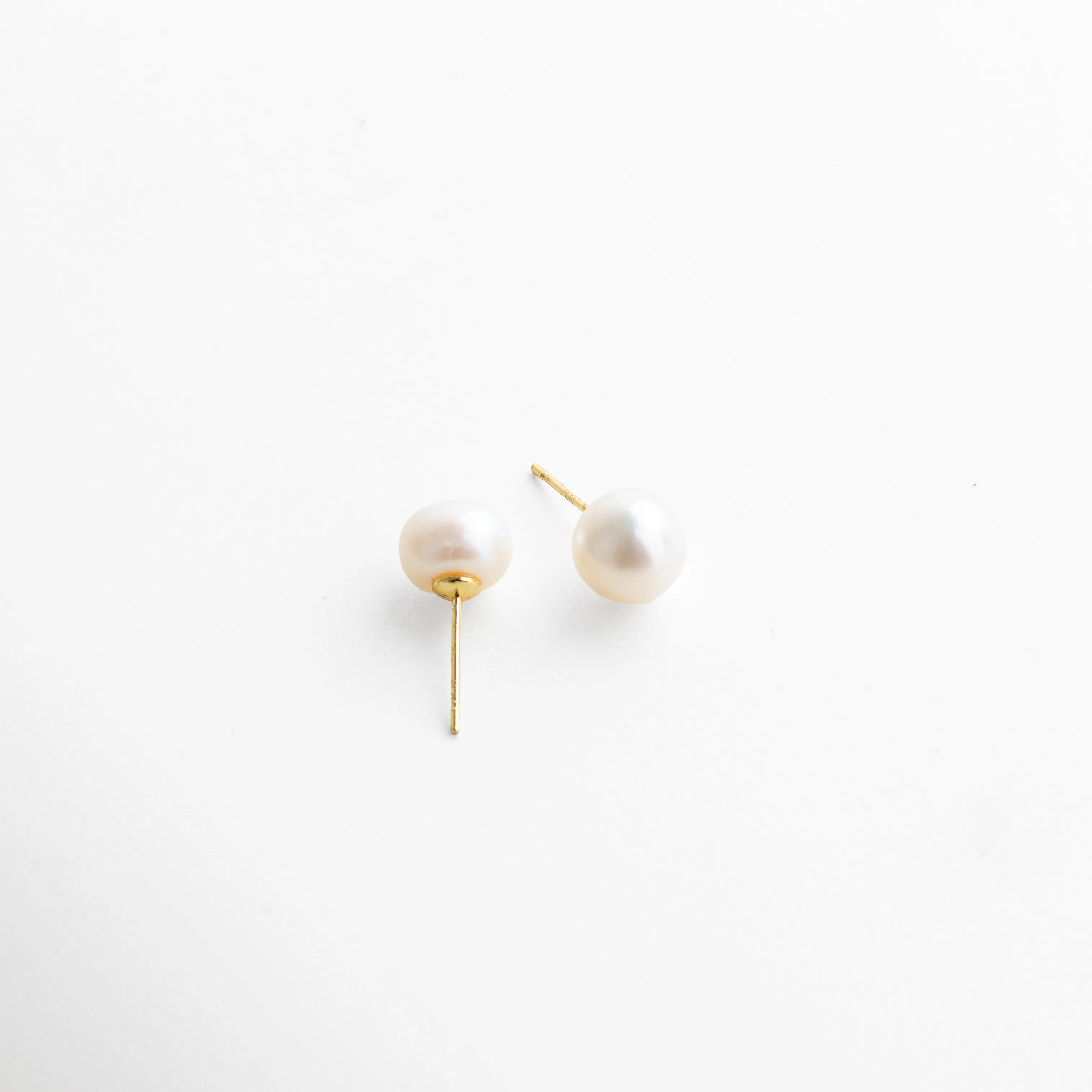 Par de aretes con perla blanca montada en base dorada, estilo atemporal que combina sencillez y sofisticación.