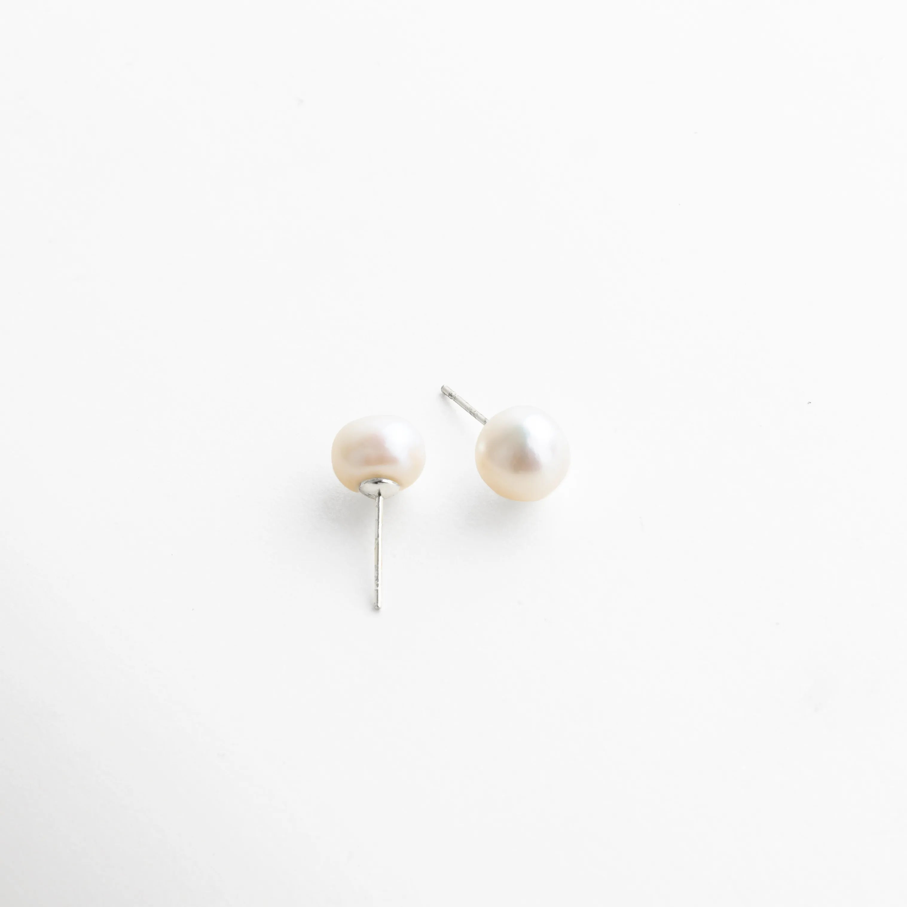 Par de aretes con perla blanca montada en base plateada, estilo atemporal que combina sencillez y sofisticación.