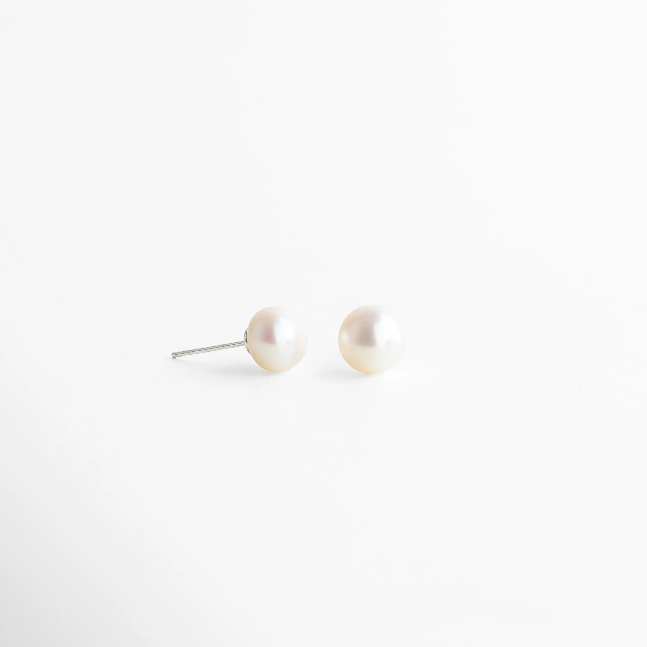 Aretes plateados con perla blanca redonda, acabado pulido y diseño refinado que destaca por su brillo natural y sutileza.
