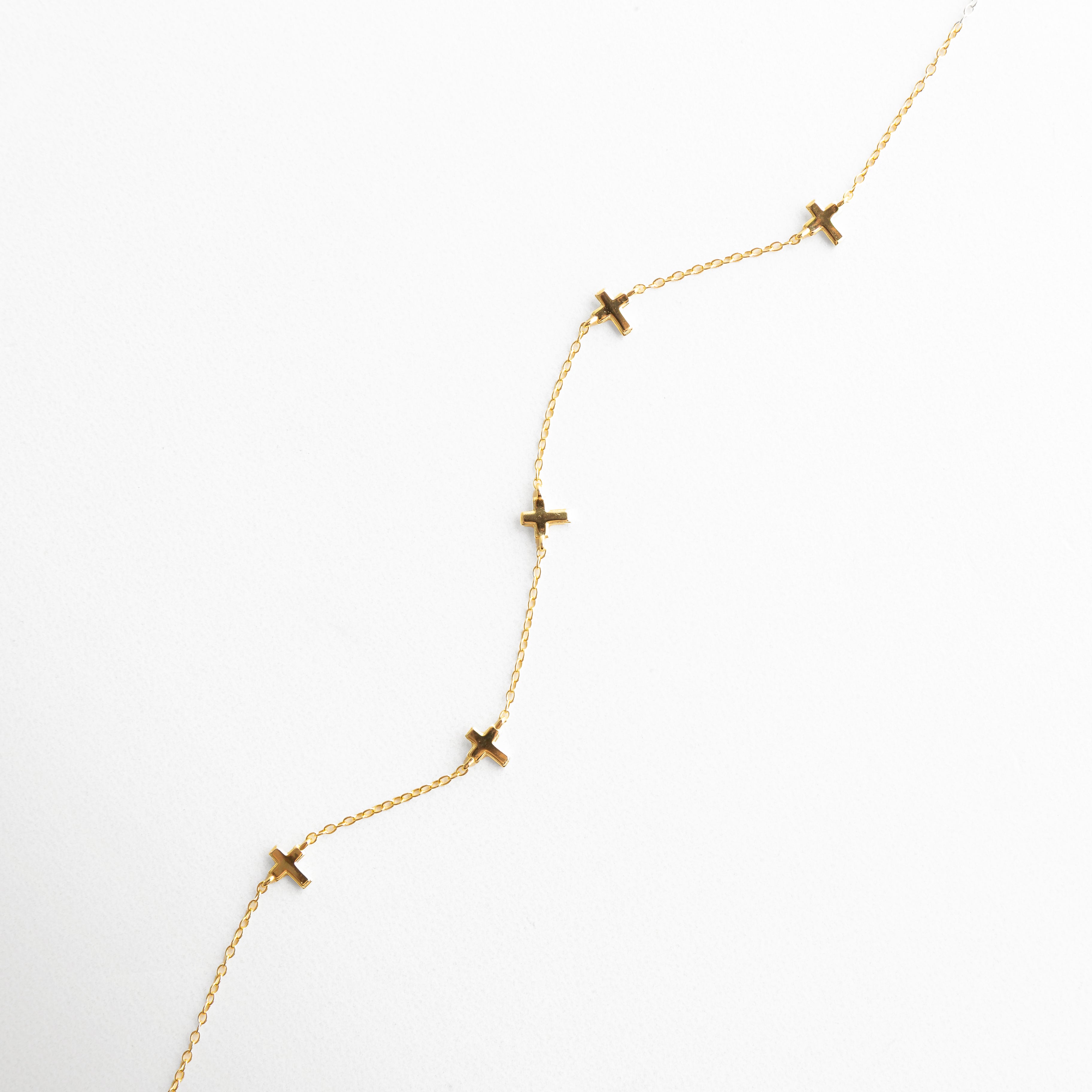 Vista en ángulo de collar dorado con dijes de cruz, mostrando la disposición armoniosa de los elementos y el acabado pulido del metal.