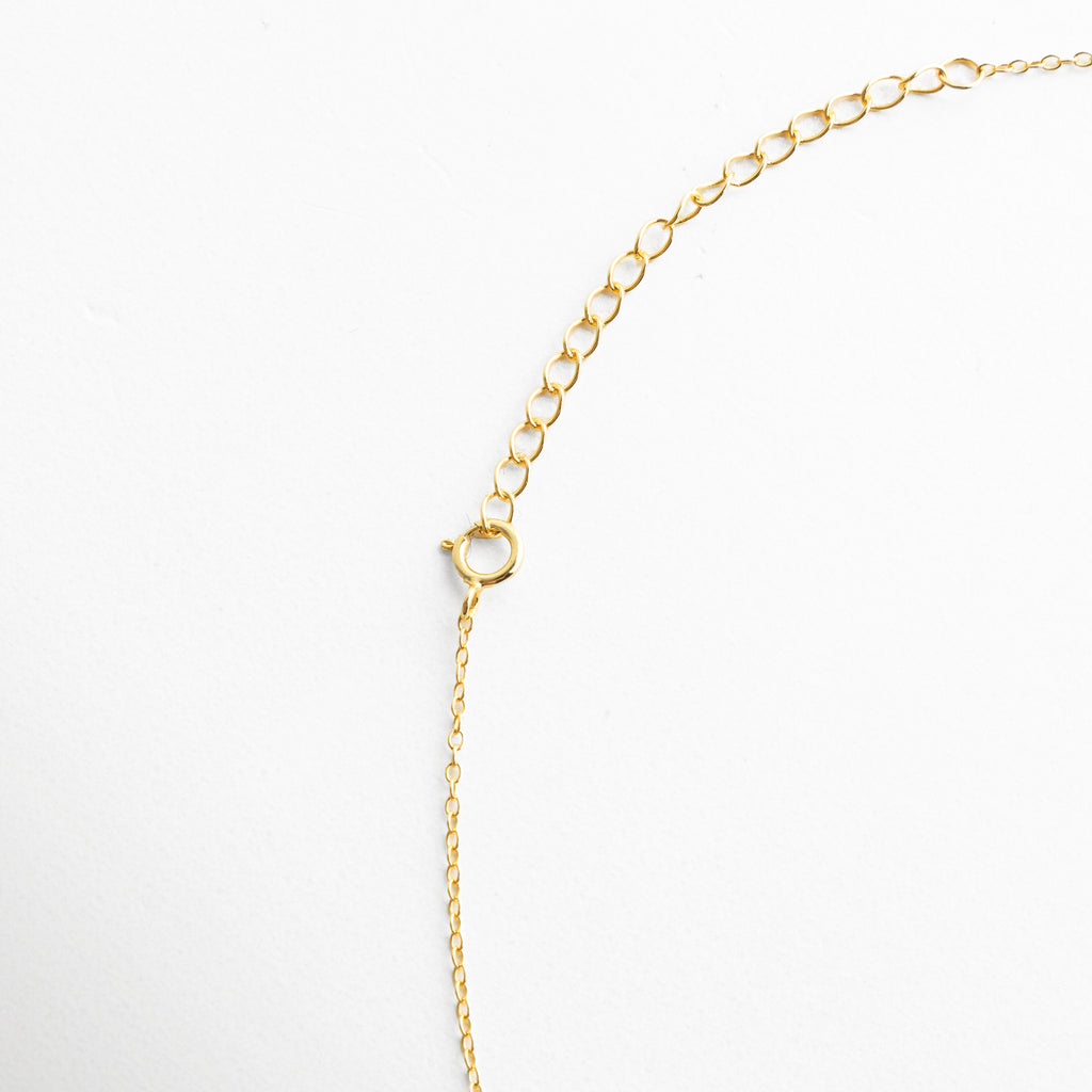 Vista detalle del collar dorado con cadena fina y broche, resaltando la textura del eslabón y el cierre discreto.