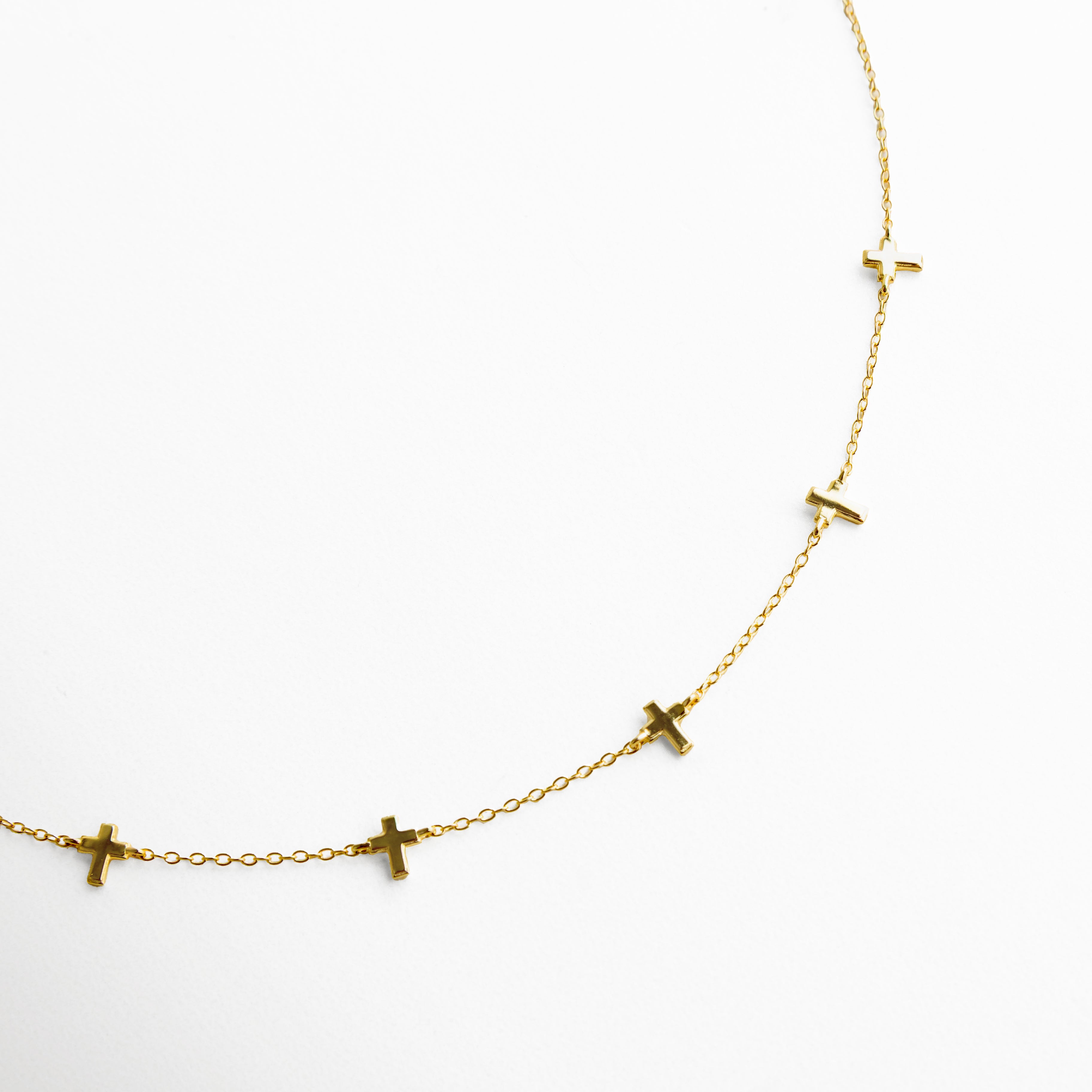 Vista cercana de collar dorado con dijes en forma de cruz, enfocando el diseño minimalista, el brillo sutil y la caída natural de la cadena.