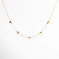 Vista frontal de collar dorado de cadena fina con pequeños dijes en forma de cruz distribuidos a lo largo del diseño, colocado sobre fondo claro, destacando su estética delicada y elegante.