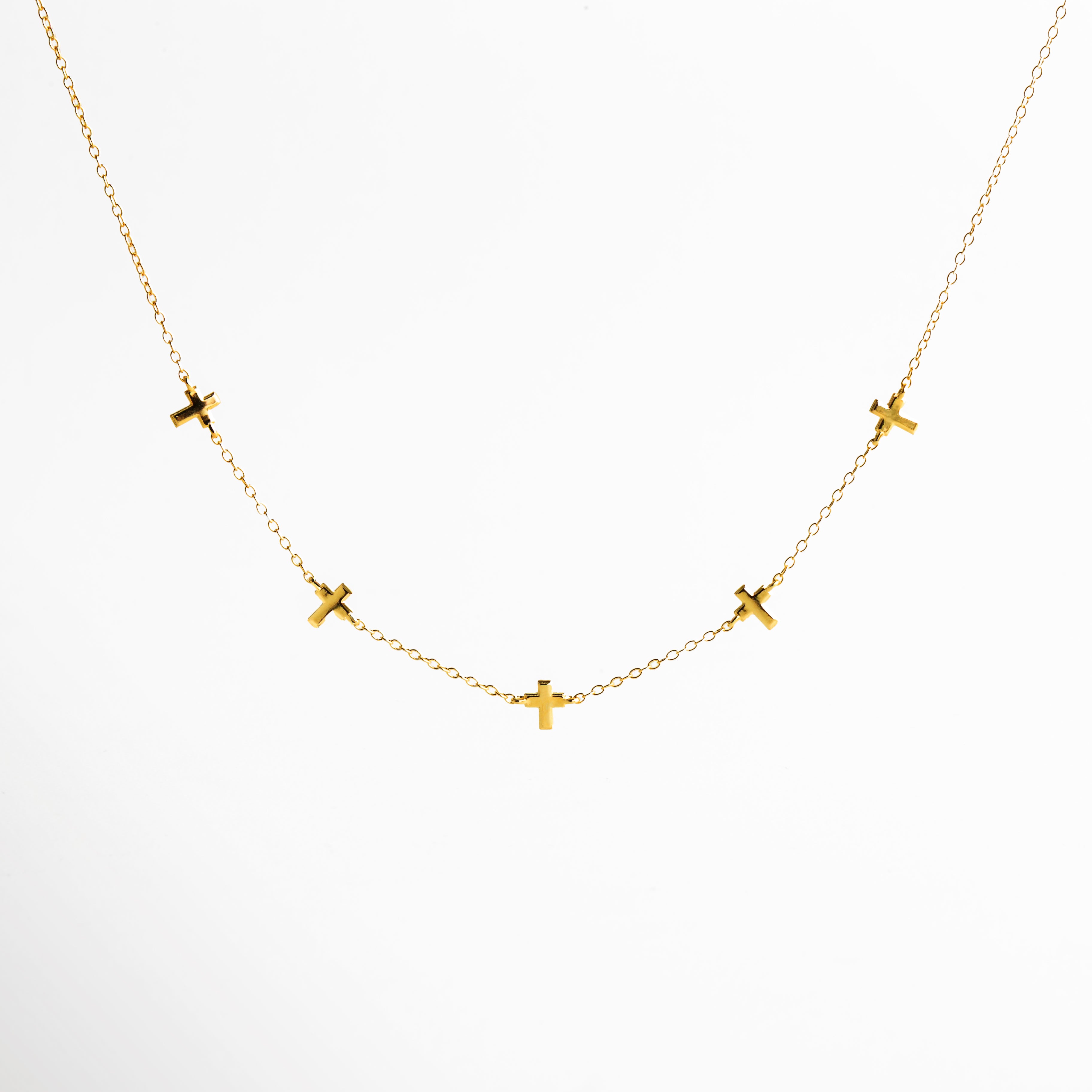 Vista frontal de collar dorado de cadena fina con pequeños dijes en forma de cruz distribuidos a lo largo del diseño, colocado sobre fondo claro, destacando su estética delicada y elegante.