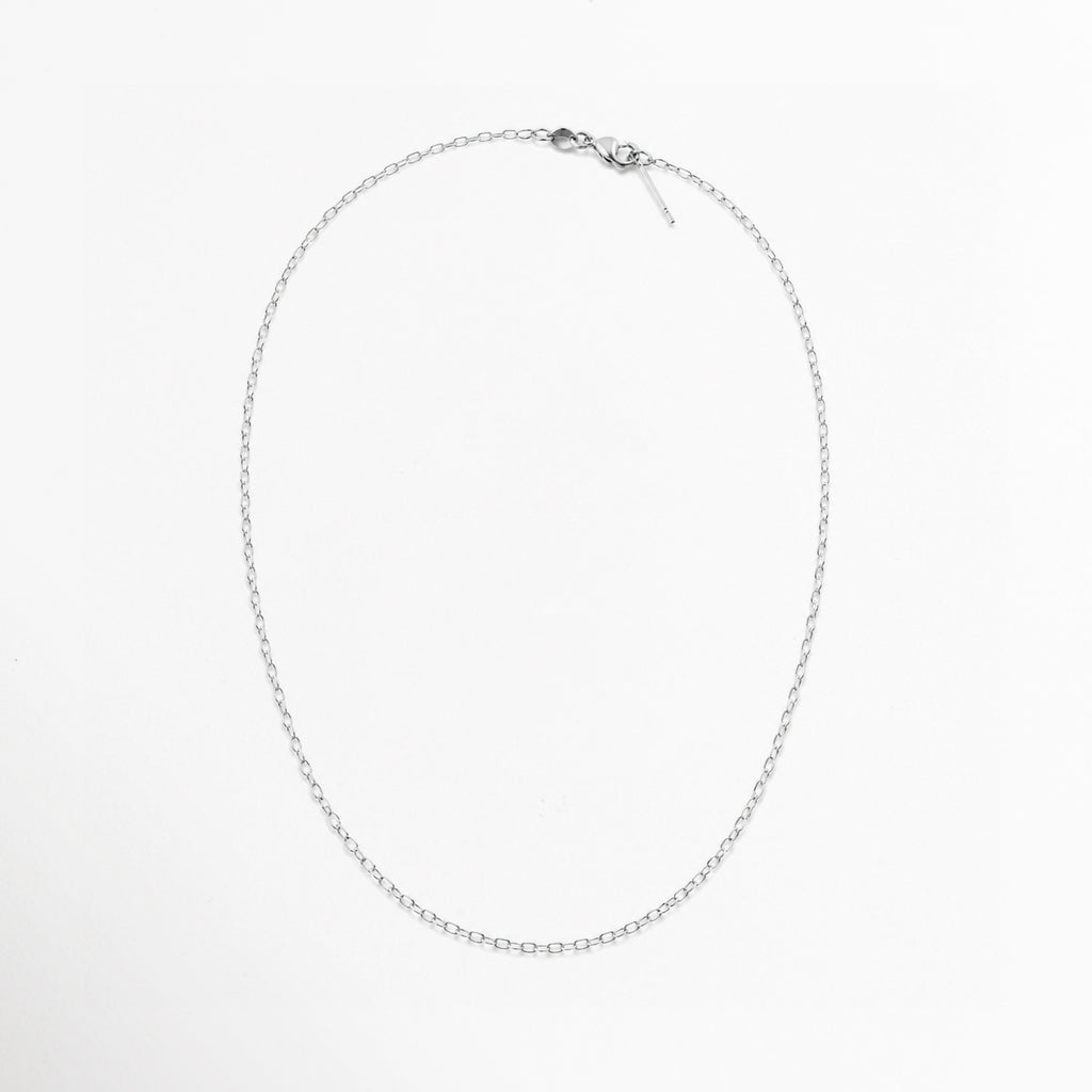 Cadena Simple Plateada dispuesta en silueta ovalada completa sobre fondo blanco mostrando su longitud de 45 cm, Vista superior de collar fino plateado cerrado con broche de reasa en la parte superior, Vista cenital de cadena de eslabones sutiles plateados alineada en forma circular/ovalada, Muestra completa de la cadena simple plateada sobre superficie neutra.