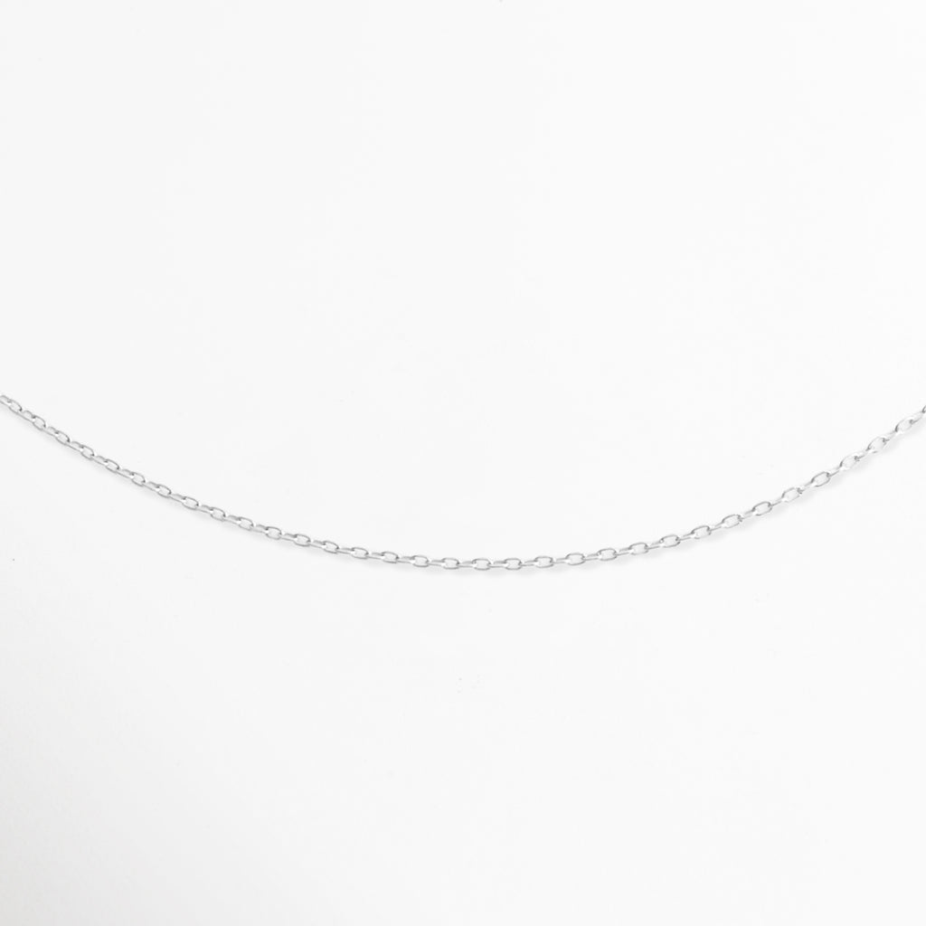 Acercamiento al tejido de eslabones finos pulidos de la Cadena Simple Plateada mostrando su brillo continuo, Vista de cerca de la caída suave y delicada del tejido de cable en tono plata, Detalle en perspectiva de la textura liviana y brillante de los eslabones metálicos plateados, Muestra macro de la curvatura e interconexión de los eslabones delgados sobre fondo claro.