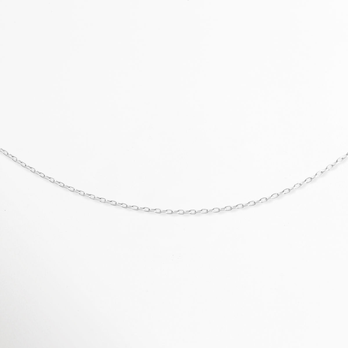 Acercamiento al tejido de eslabones finos pulidos de la Cadena Simple Plateada mostrando su brillo continuo, Vista de cerca de la caída suave y delicada del tejido de cable en tono plata, Detalle en perspectiva de la textura liviana y brillante de los eslabones metálicos plateados, Muestra macro de la curvatura e interconexión de los eslabones delgados sobre fondo claro.