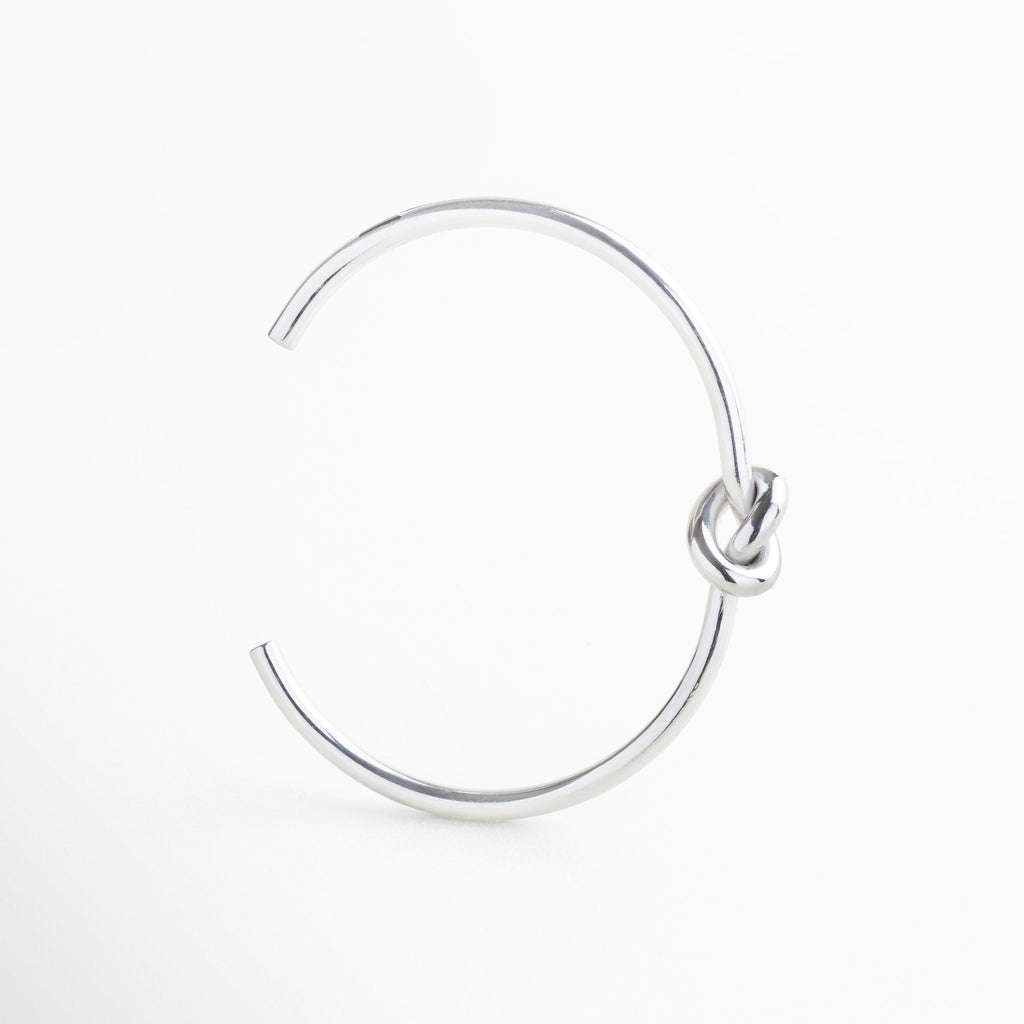 Pulsera rígida de 0.3 cm de ancho con diseño delgado, Proporción sutil del brazalete con nudo central, Joya plateada de diseño delgado y acabado pulido, Pulsera liviana con estructura firme y elegante
