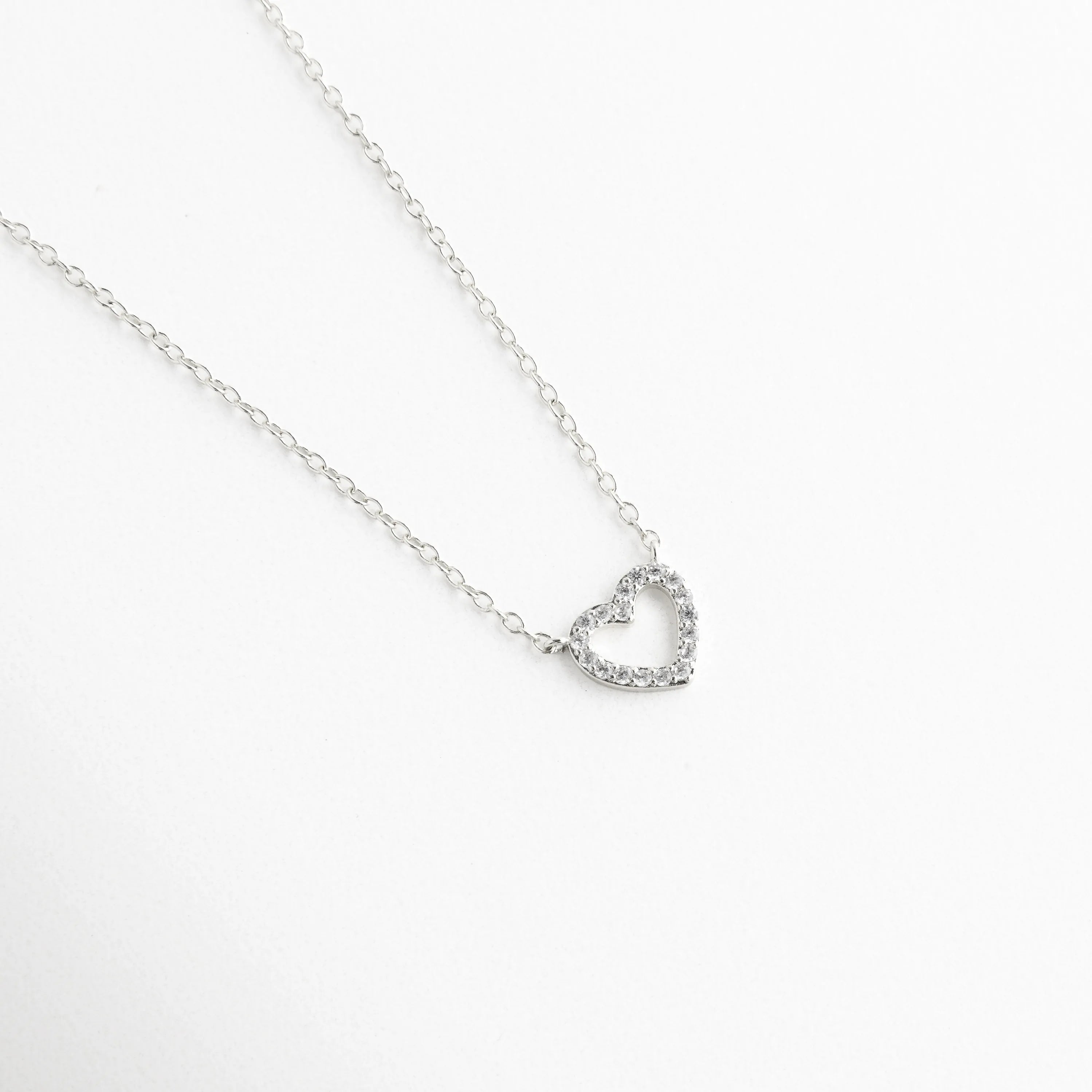 detalle de dije de corazón plateado, corazón plateado con acabado pulido, collar elegante con dije minimalista, joyería fina de estética limpia, dije de corazón sofisticado plateado, collar femenino contemporáneo