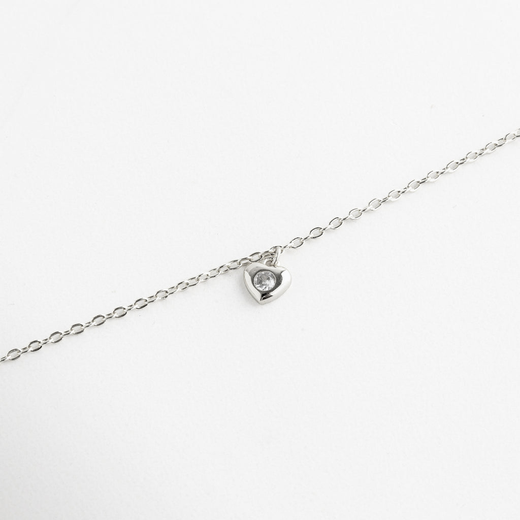 Perfil del dije de corazón colgante, Caída natural del collar con movimiento sutil, Dije de corazón visto desde ángulo lateral, Diseño ligero del collar con dije suspendido, Espesor del dije y unión con la cadena