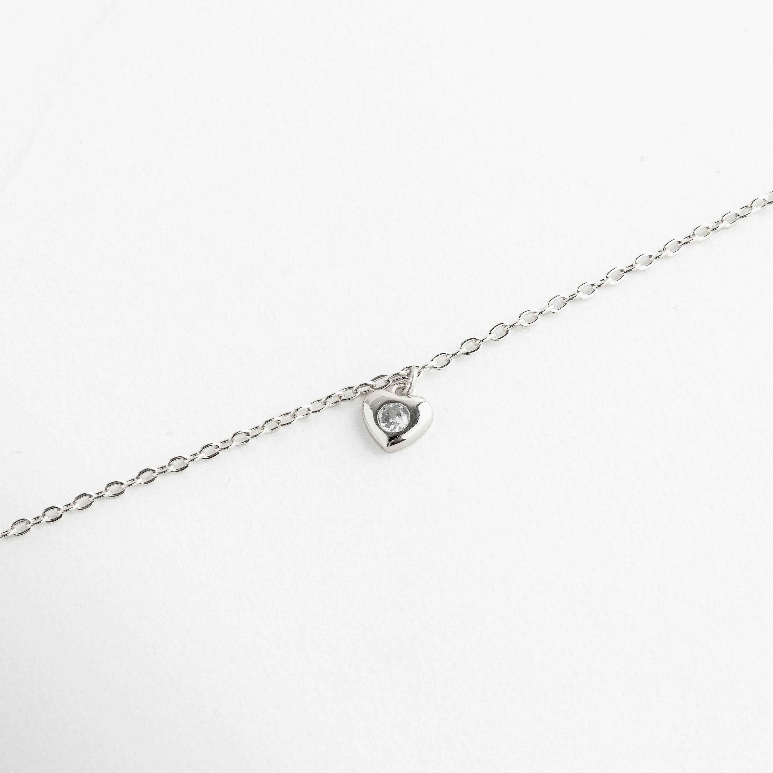 Perfil del dije de corazón colgante, Caída natural del collar con movimiento sutil, Dije de corazón visto desde ángulo lateral, Diseño ligero del collar con dije suspendido, Espesor del dije y unión con la cadena