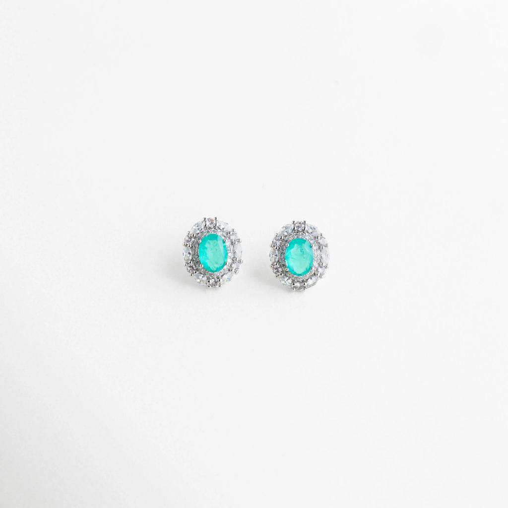 Par de aretes tipo broquel ovalados con piedras color turquesa y marco brillante, Pendientes de diseño clásico con gemas azul neón y halo de cristales para mujer, Detalle frontal de aretes ovalados con piedras de imitación Paraiba vibrantes, Aretes pequeños de lujo con piedras facetadas color turquesa y borde de zirconias, Par de pendientes elegantes con brillo excepcional y gema central azul aqua.