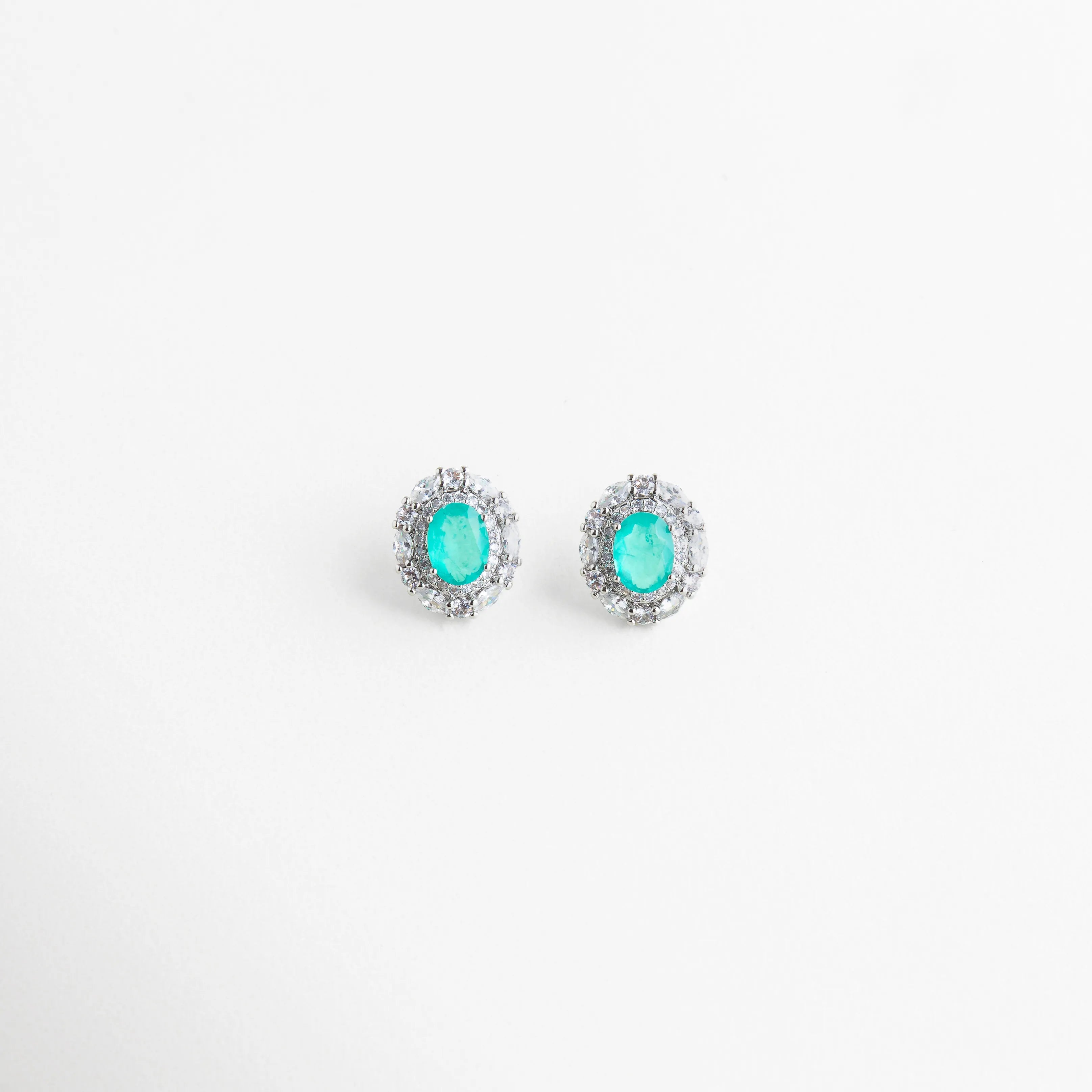 Par de aretes tipo broquel ovalados con piedras color turquesa y marco brillante, Pendientes de diseño clásico con gemas azul neón y halo de cristales para mujer, Detalle frontal de aretes ovalados con piedras de imitación Paraiba vibrantes, Aretes pequeños de lujo con piedras facetadas color turquesa y borde de zirconias, Par de pendientes elegantes con brillo excepcional y gema central azul aqua.