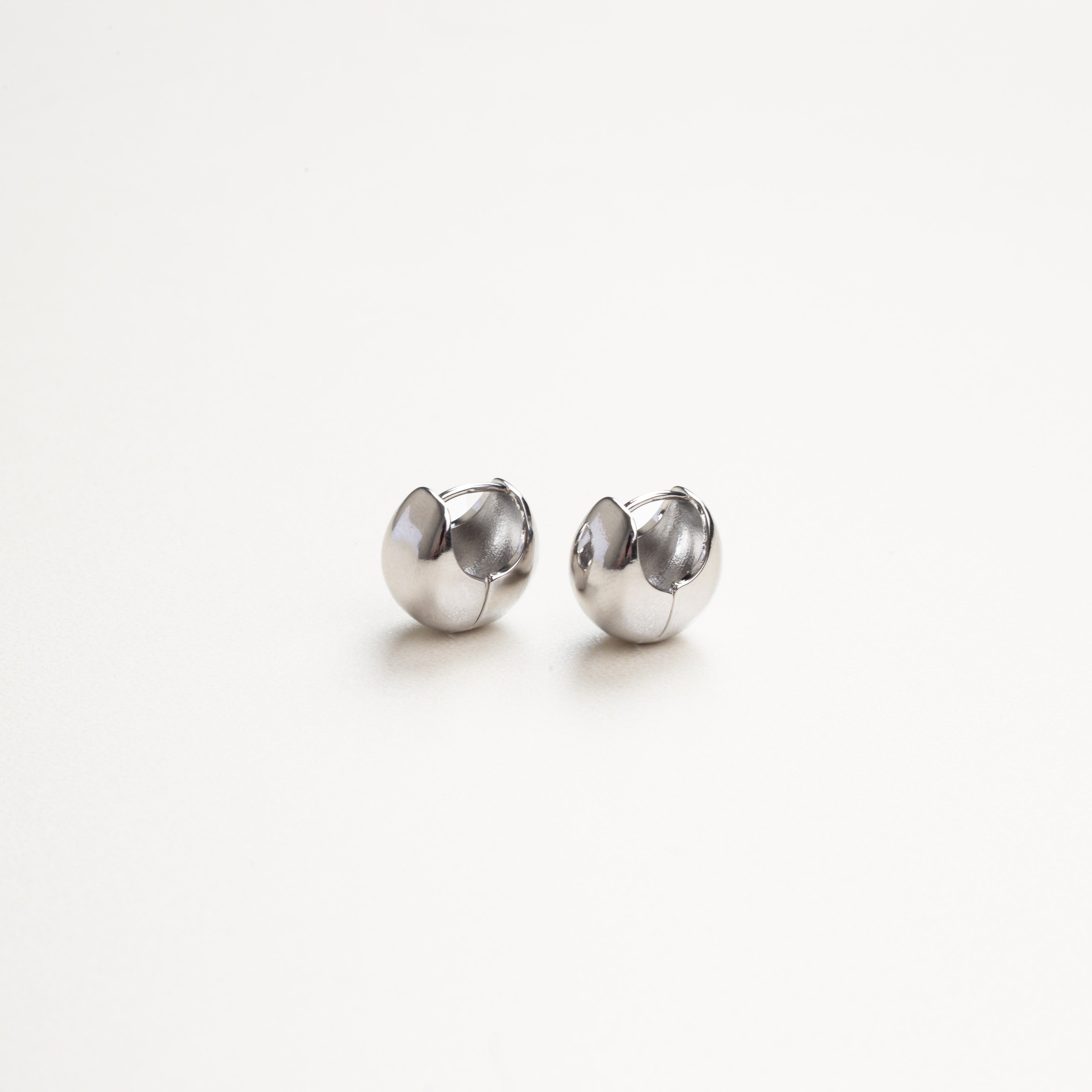 Aretes sencillos en acabado plateado vistos de lado, estilo discreto y moderno