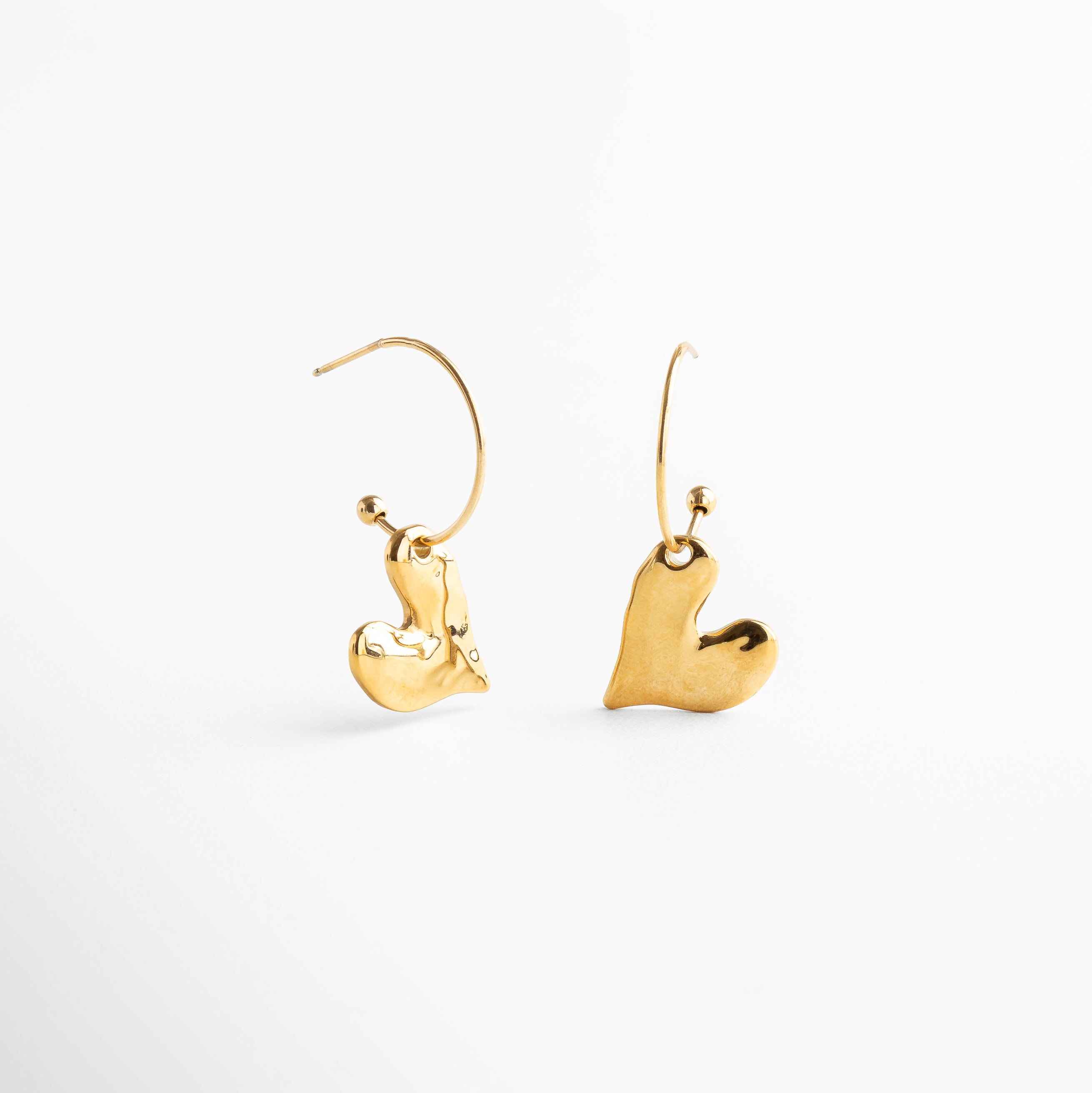 Detalle del diseño orgánico de corazón dorado, Primer plano del acabado pulido en forma de corazón, Textura lisa y curva de los aretes Amour, Diseño fluido en dorado con silueta romántica