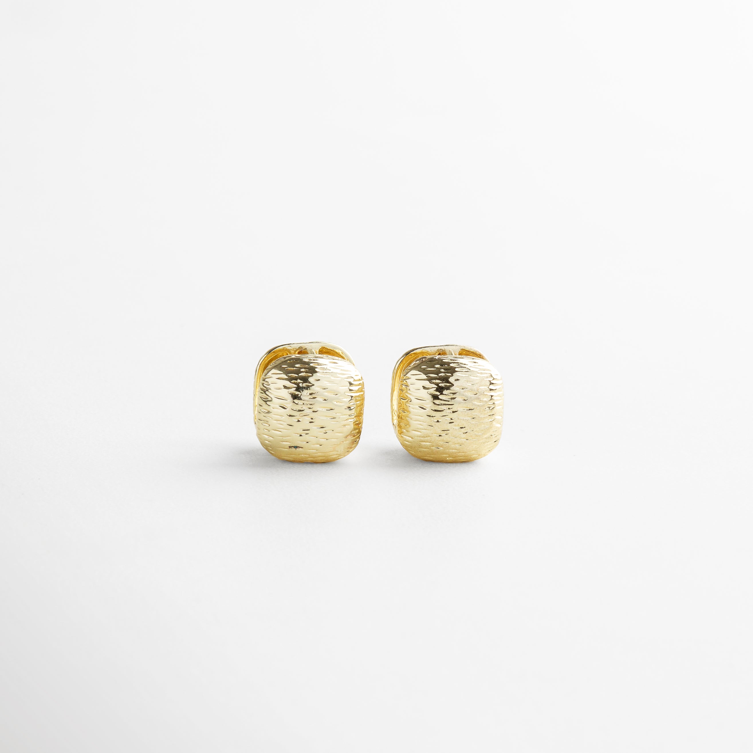 Aretes Valentines dorados vistos de frente, con forma cuadrada y textura rayada irregular sobre acabado brillante. Vista frontal de los aretes pequeños en chapa de oro 18K, con diseño texturizado y forma geométrica. Primer plano de los Aretes Valentines dorados, destacando su sutil brillo y textura artesanal. Par de aretes dorados con diseño cuadrado y acabado rayado visto desde el frente. Aretes en forma de cuadro pequeño con textura irregular, perfectos para complementar un look diar
