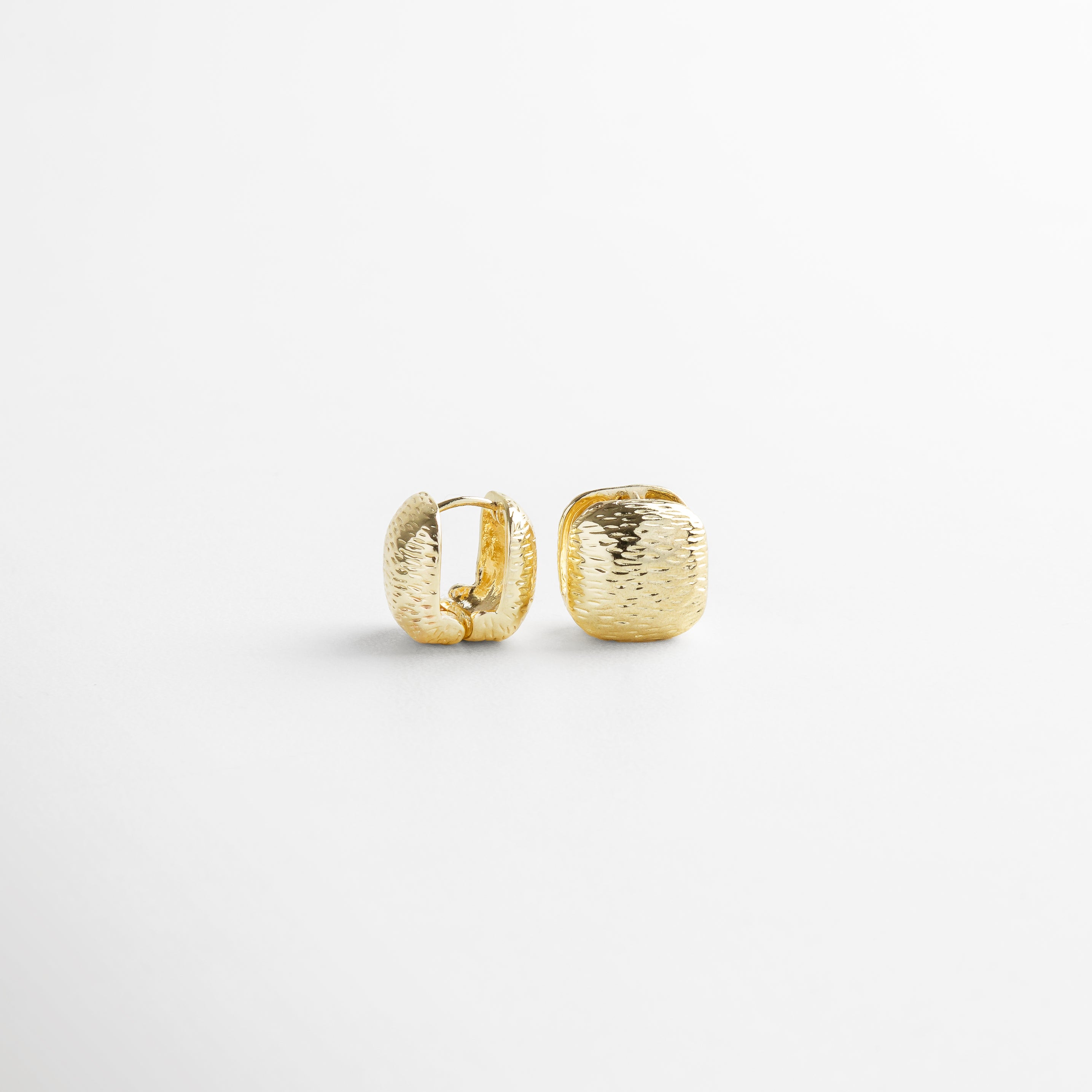 Aretes Valentines dorados vistos de perfil, mostrando su espesor sutil y textura en relieve. Detalle lateral de los aretes cuadrados con acabado rayado y forma moderna en chapa de oro. Vista de lado de los Aretes Valentines, resaltando su diseño pequeño y textura tridimensional. Arete dorado visto de perfil, con forma cuadrada y superficie irregular que capta la luz con discreción. Perfil del arete con textura de rayas irregulares y acabado dorado brillante, ideal para un look versátil.