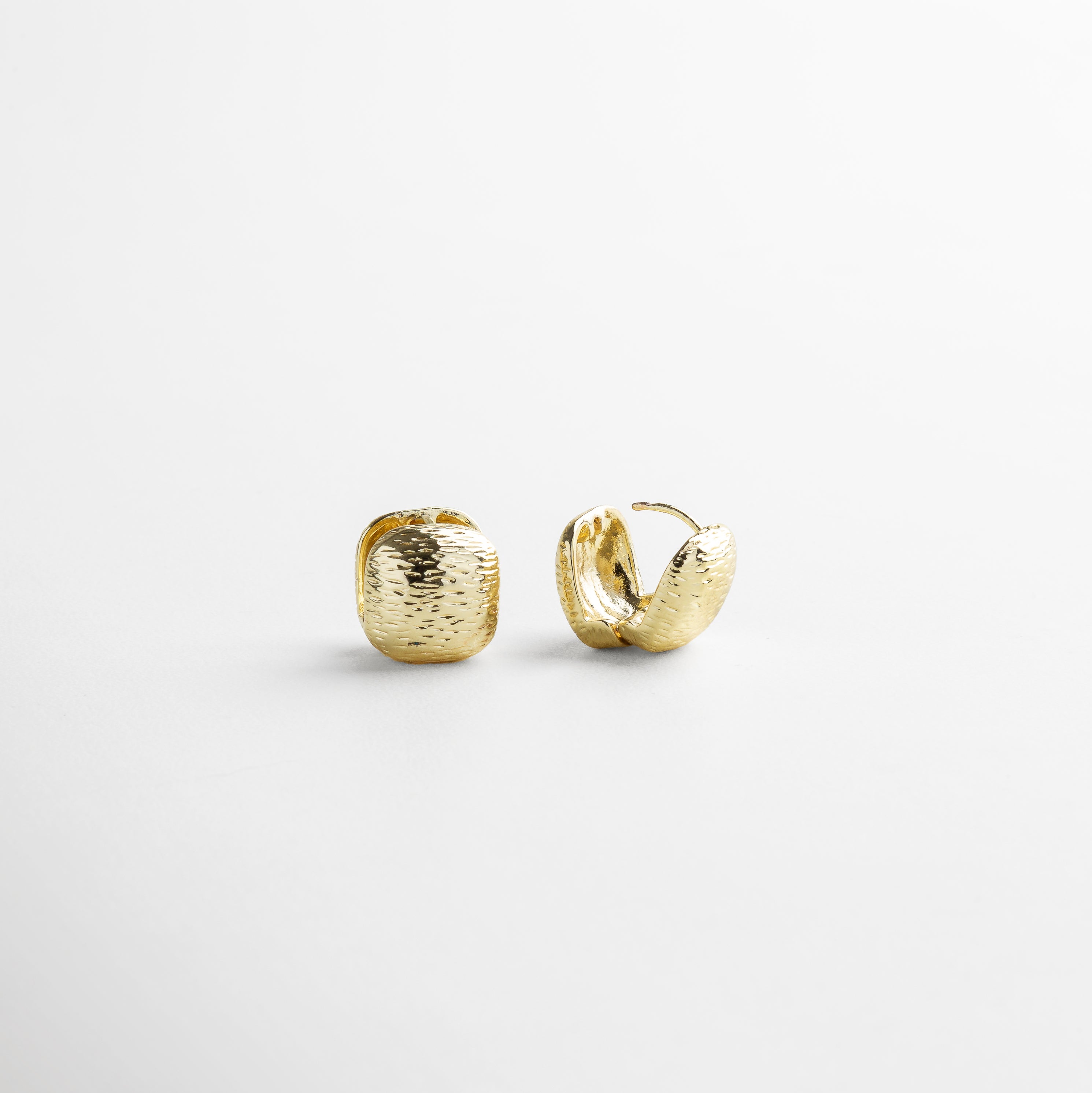Vista superior de los Aretes Valentines dorados, mostrando su forma cuadrada de 2 cm x 1 cm y textura rayada. Aretes de chapa de oro 18K vistos desde arriba, resaltando la superficie texturizada y forma simétrica. Toma cenital de los aretes Valentines dorados, con acabado irregular y diseño minimalista con carácter. Aretes dorados vistos desde arriba, ideales para combinar con otros accesorios dorados delicados. Vista superior de par de aretes pequeños cuadrados con textura tipo rayas en ton