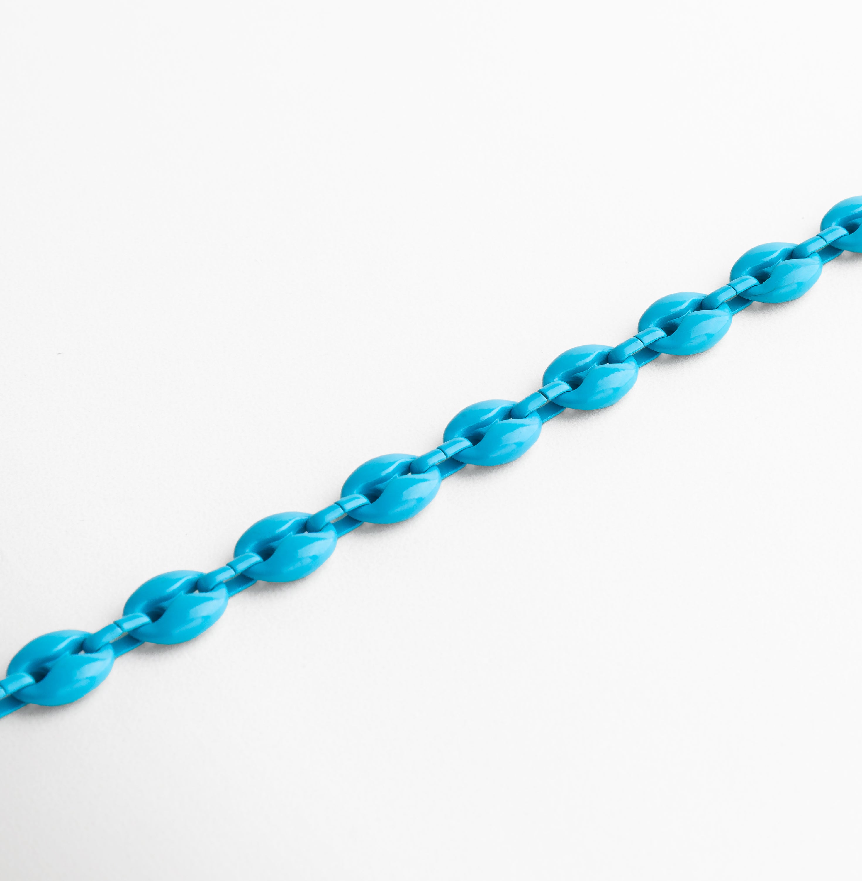 Pulsera azul vista en ángulo resaltando su color suave, Diseño fluido con eslabones en azul celeste y dorado, Secuencia de eslabones acrílicos en perspectiva, Contraste sutil entre el azul claro y el metal