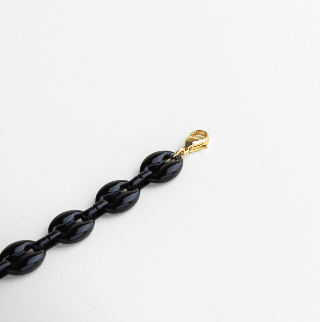 Detalle de eslabones acrílicos negros de acabado pulido, Cierre dorado de chapa de oro 18K con textura brillante, Unión entre acrílico negro y metal dorado, Superficie lisa y brillante del acrílico en tono negro