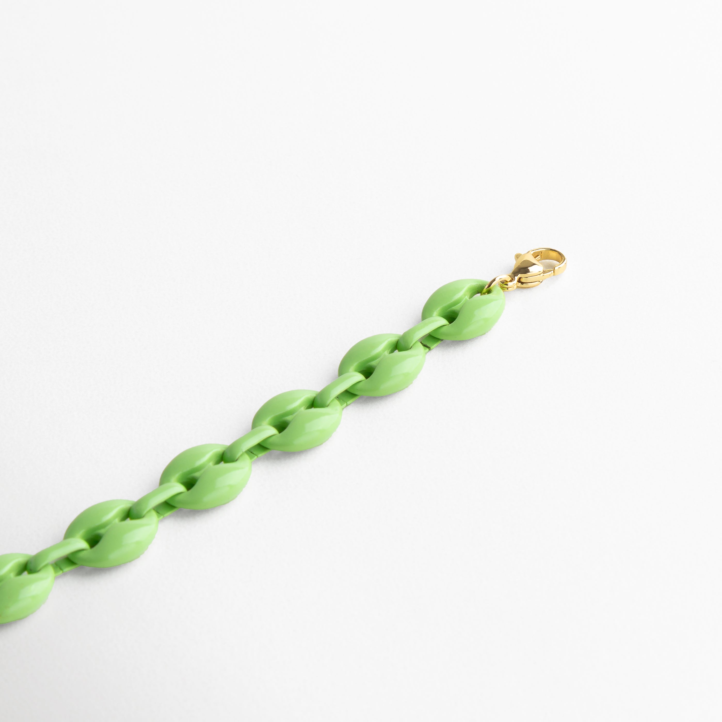Pulsera verde vista en ángulo resaltando el color suave, Secuencia de eslabones en verde claro con contraste dorado, Perspectiva del diseño moderno y ligero, Vista del juego de luces en el acrílico verde