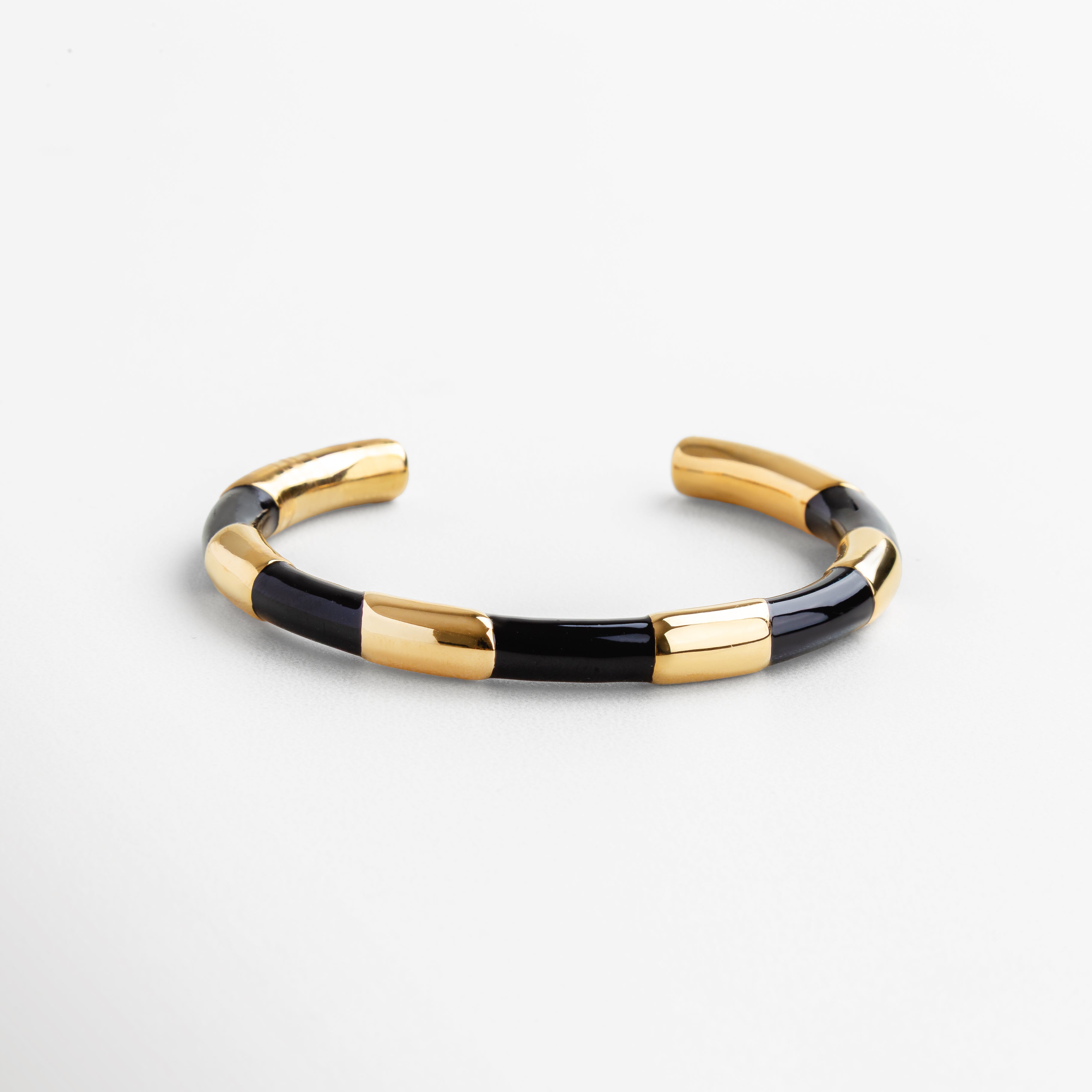 Detalle del acabado dorado con inserciones negras, Textura pulida en dorado y esmalte negro, Primer plano del contraste dorado-negro en pulsera rígida, Detalles geométricos en negro sobre fondo dorado