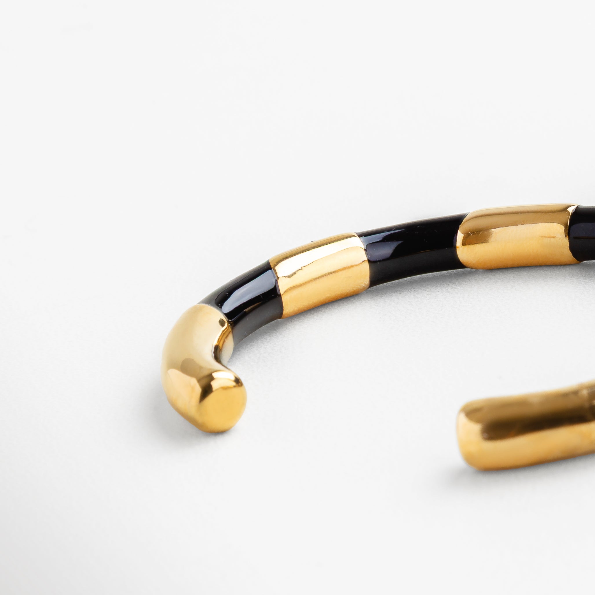 Pulsera rígida vista en ángulo con diseño dorado y negro, Perfil moderno de brazalete dorado con esmalte negro, Vista lateral del contraste entre dorado brillante y negro opaco, Ángulo de diseño gráfico en negro sobre estructura dorada