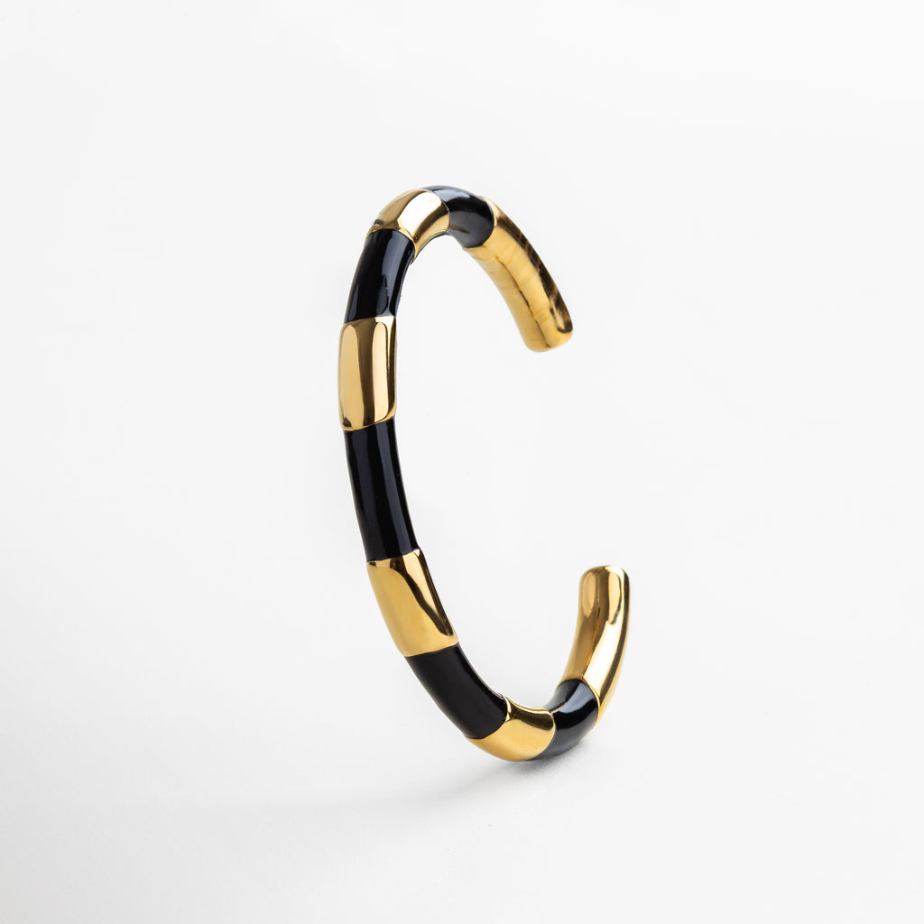 Pulsera rígida dorada con detalles en negro, Brazalete dorado con contraste en negro elegante, Joya dorada tipo cuff con esmalte negro, Pulsera dorada con diseño gráfico en negro