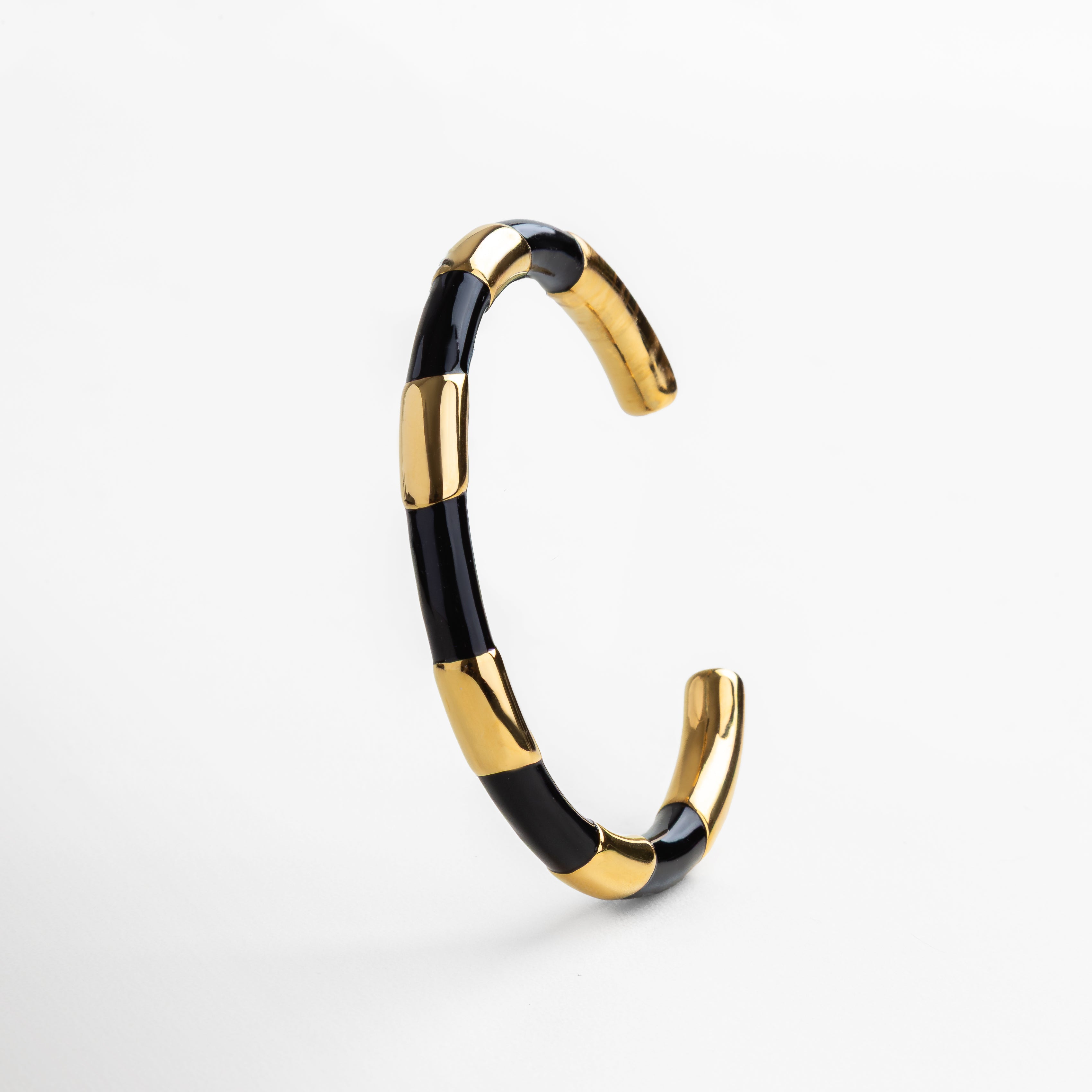 Pulsera rígida dorada con detalles en negro, Brazalete dorado con contraste en negro elegante, Joya dorada tipo cuff con esmalte negro, Pulsera dorada con diseño gráfico en negro