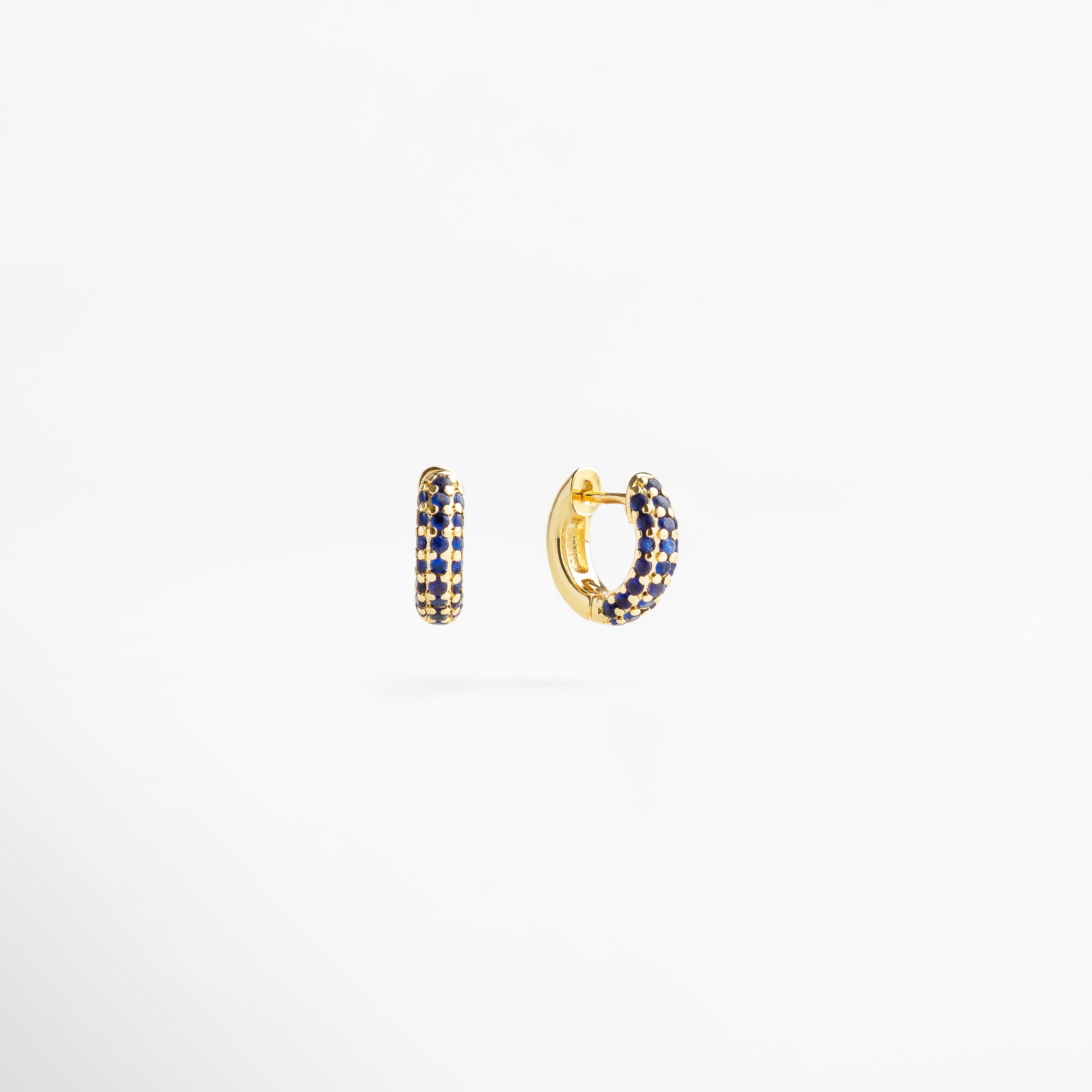aretes dorados con zirconias azul zafiro, diseño moderno y elegante, destellos profundos y sofisticados, joyería que realza la mirada, accesorios chic y llenos de estilo