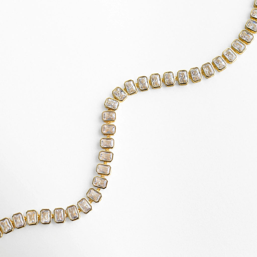 Collar Jung Golden en forma ondulada mostrando flexibilidad y brillo de zirconias, Detalle de collar dorado con piedras cuadradas en movimiento suave, Vista curva de collar con zirconias cúbicas y acabado pulido brillante, Collar elegante con diseño fluido y piedras alineadas en tono oro 18K, Detalle dinámico de collar tipo tenis con zirconias reflejando la luz
