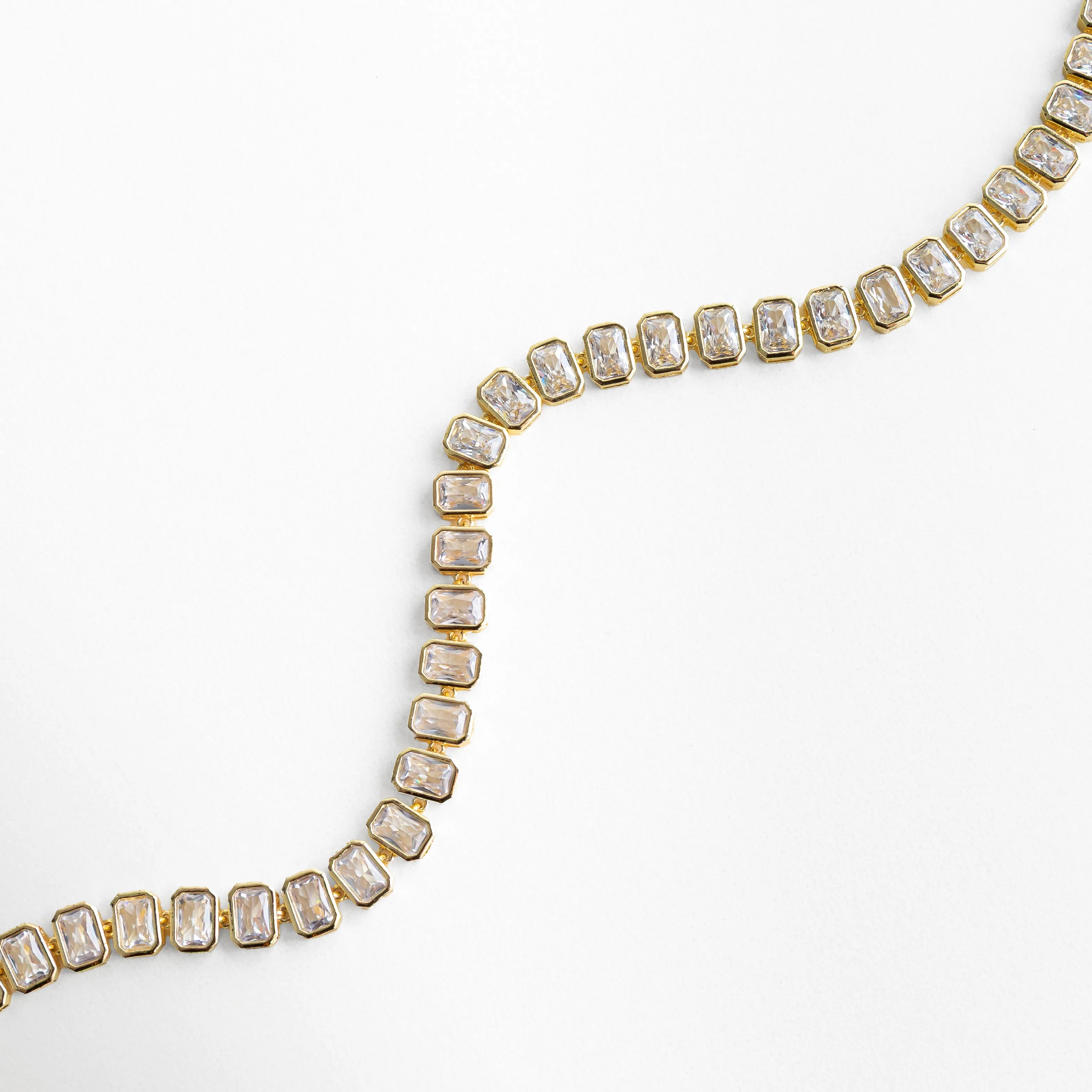 Collar Jung Golden en forma ondulada mostrando flexibilidad y brillo de zirconias, Detalle de collar dorado con piedras cuadradas en movimiento suave, Vista curva de collar con zirconias cúbicas y acabado pulido brillante, Collar elegante con diseño fluido y piedras alineadas en tono oro 18K, Detalle dinámico de collar tipo tenis con zirconias reflejando la luz