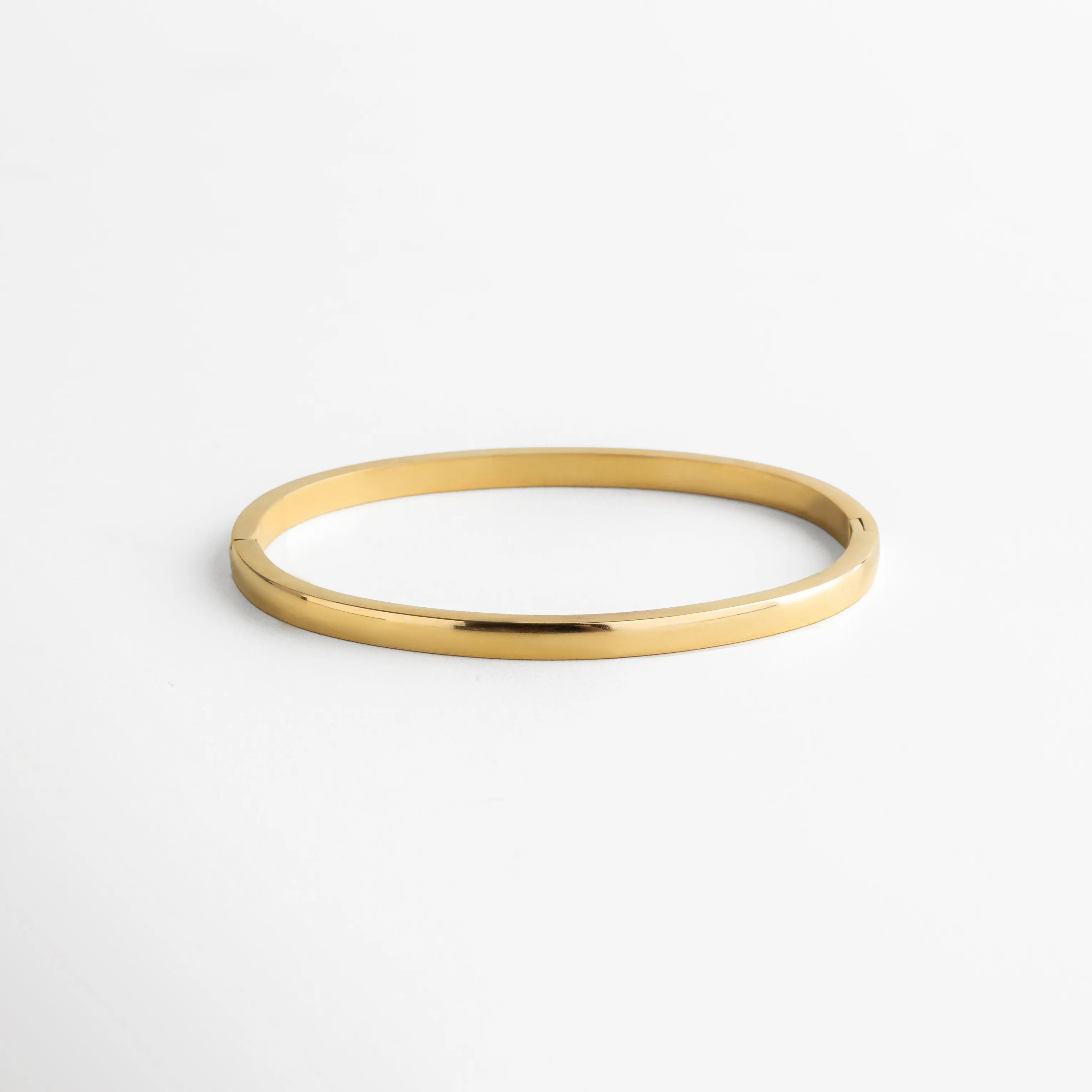 Pulsera dorada de superficie lisa y pulida, vista desde el reverso para resaltar su acabado impecable y su forma ovalada que se adapta con suavidad a la muñeca. La imagen transmite una sensación de lujo discreto y atención al detalle.