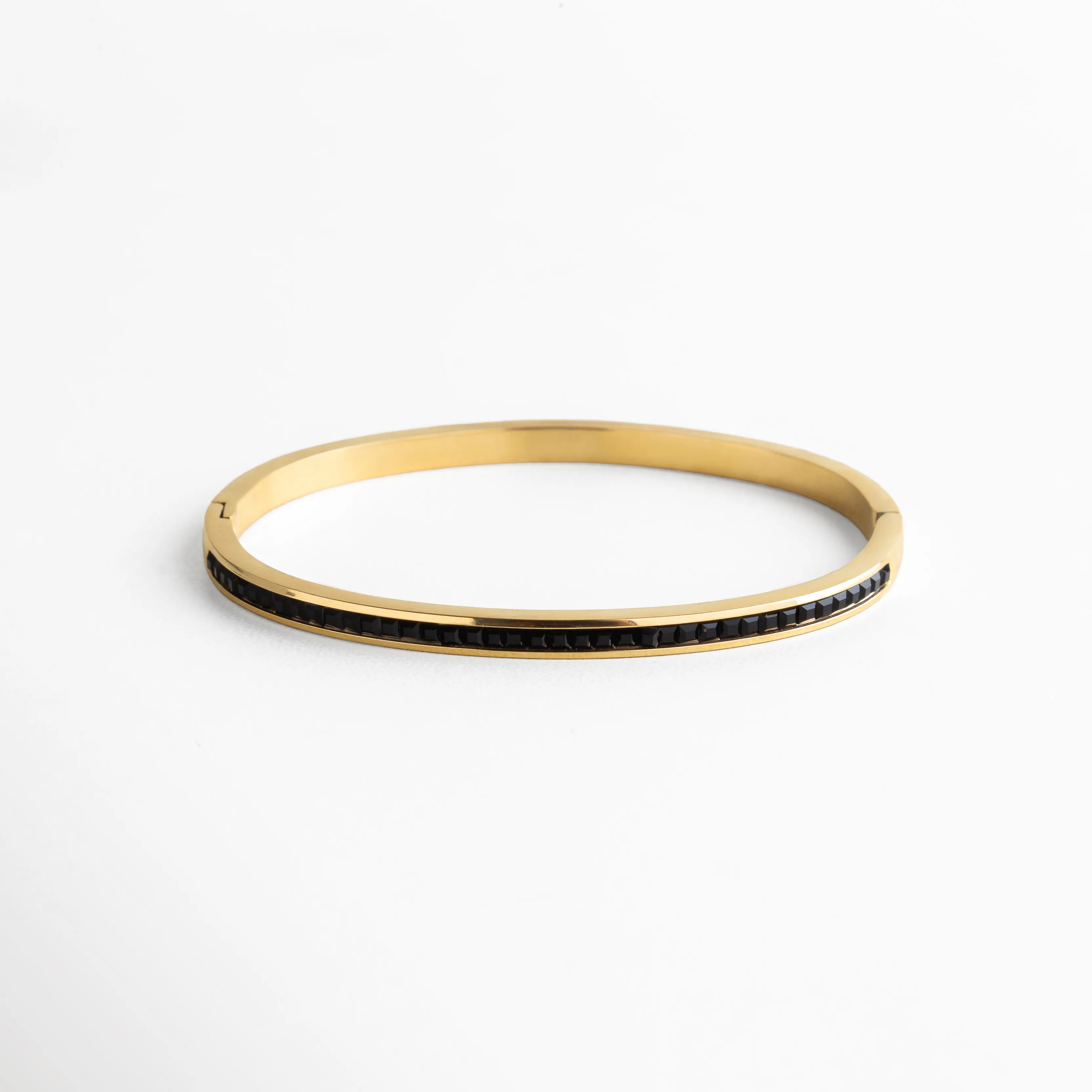 Pulsera rígida dorada con un delicado canal de zirconias negras incrustadas que recorren su superficie con elegancia. El contraste entre el dorado pulido y el brillo oscuro de las piedras aporta un toque sofisticado y moderno, ideal para complementar tanto looks de noche como atuendos minimalistas de día.