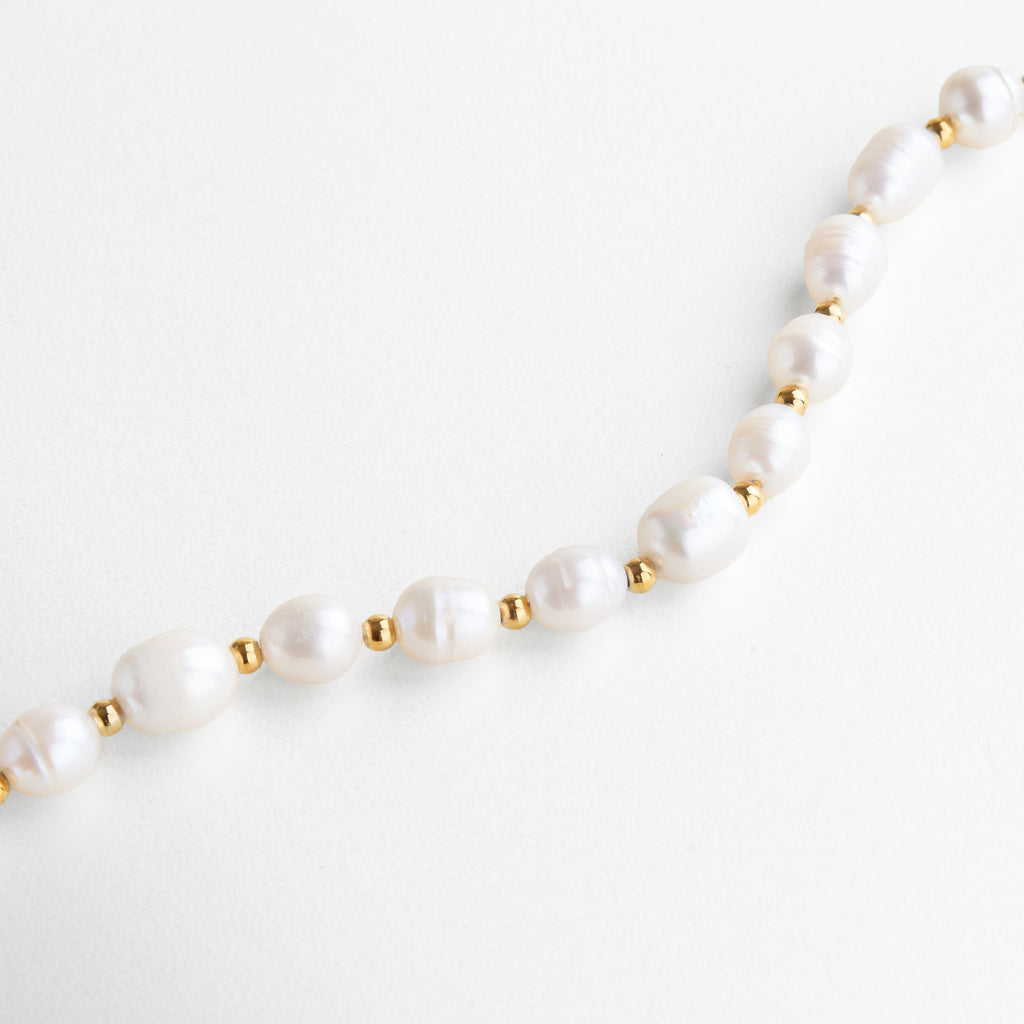 perlas de agua de imitación engastadas con brillo suave, superficie lisa y delicada, acabado dorado que realza su luminosidad, detalle refinado y elegante, diseño pensado para uso diario