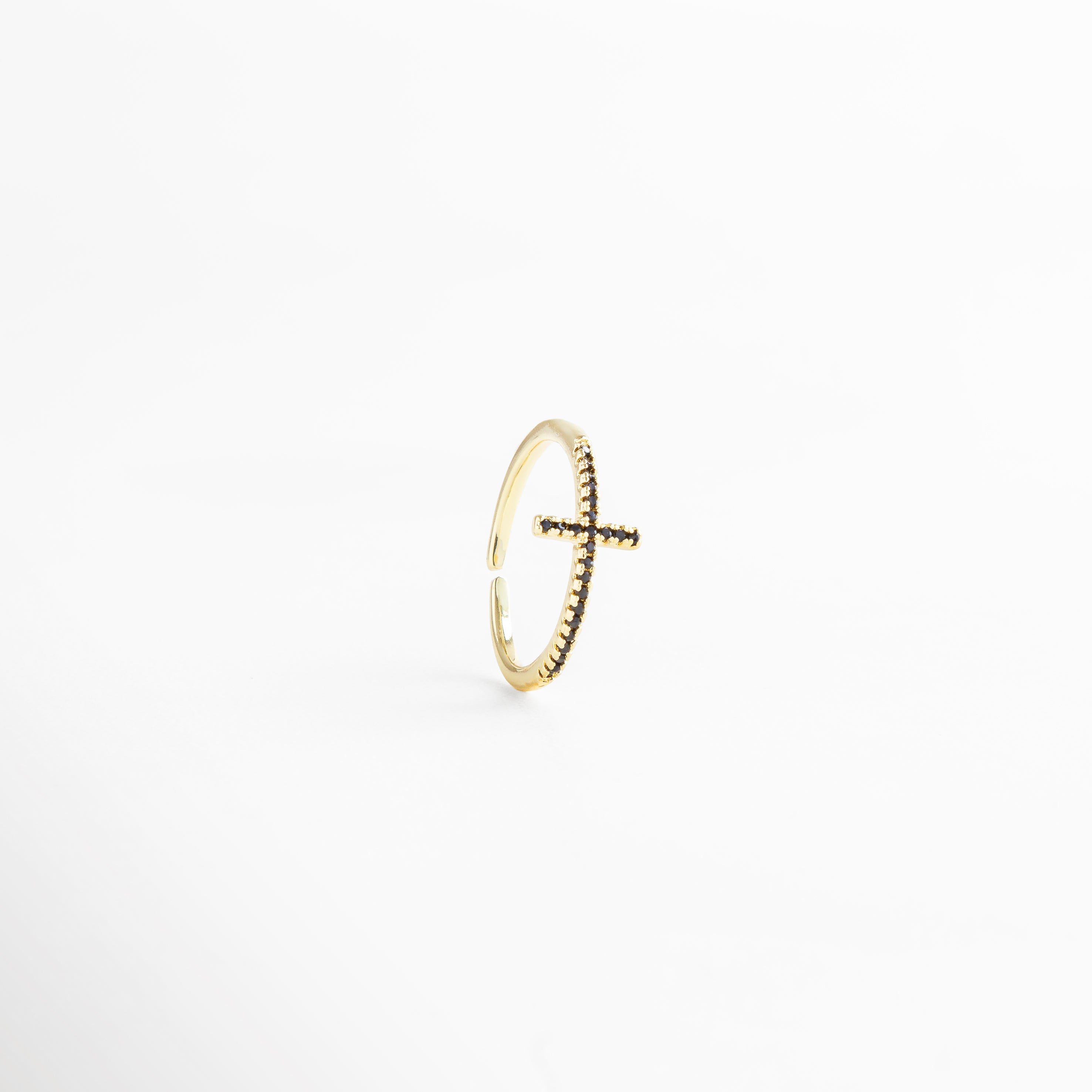 Anillo dorado ajustable con cruz al frente, bañado en Oro 18K e incrustado con zirconias negras, resaltando su brillo elegante.