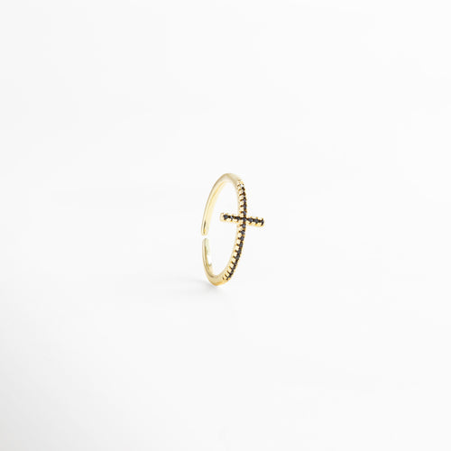 Anillo dorado ajustable con cruz al frente, bañado en Oro 18K e incrustado con zirconias negras, resaltando su brillo elegante.