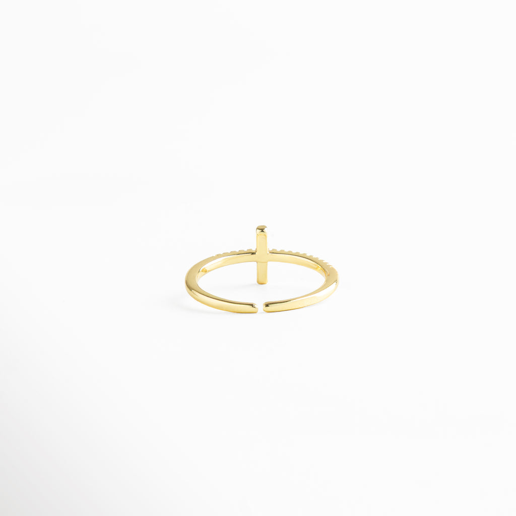 Anillo dorado minimalista con cruz de zirconias negras, fotografiado en ángulo diagonal para resaltar su brillo y estilo ajustable.