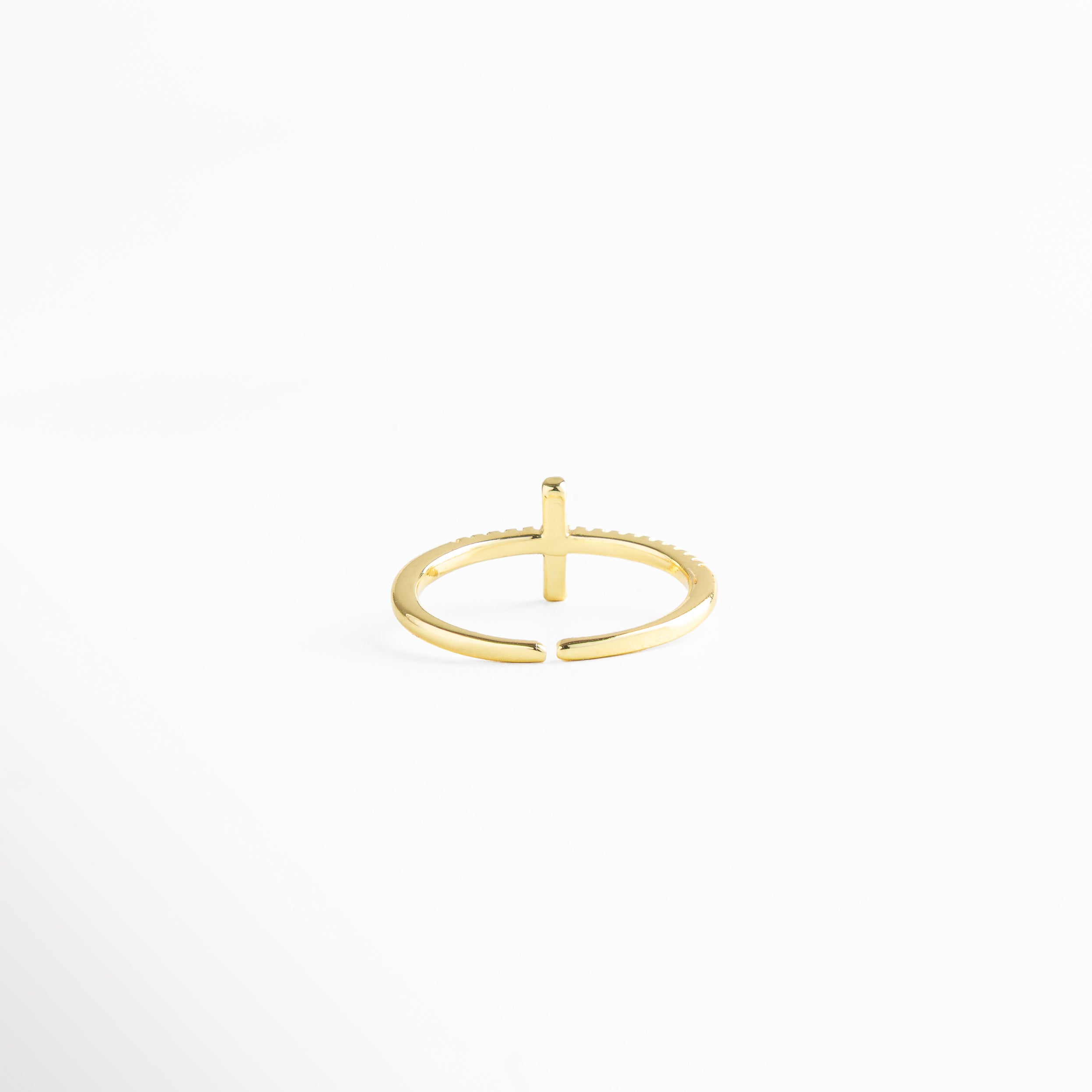 Anillo dorado minimalista con cruz de zirconias negras, fotografiado en ángulo diagonal para resaltar su brillo y estilo ajustable.