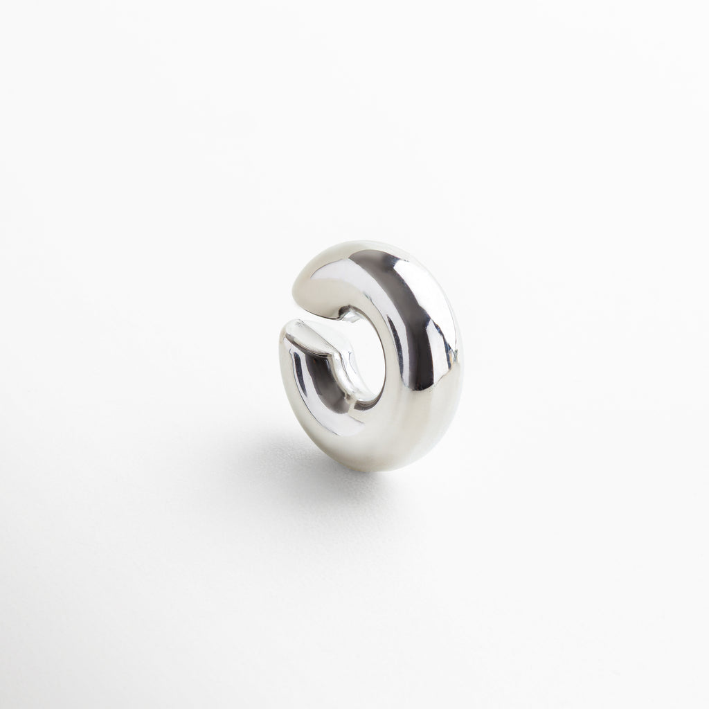 Detalle de ear cuff plateado con acabado brillante y pulido, Primer plano de accesorio para oreja en acero inoxidable, Textura y brillo del ear cuff plateado sin perforación, Diseño contemporáneo en acero inoxidable con baño plateado