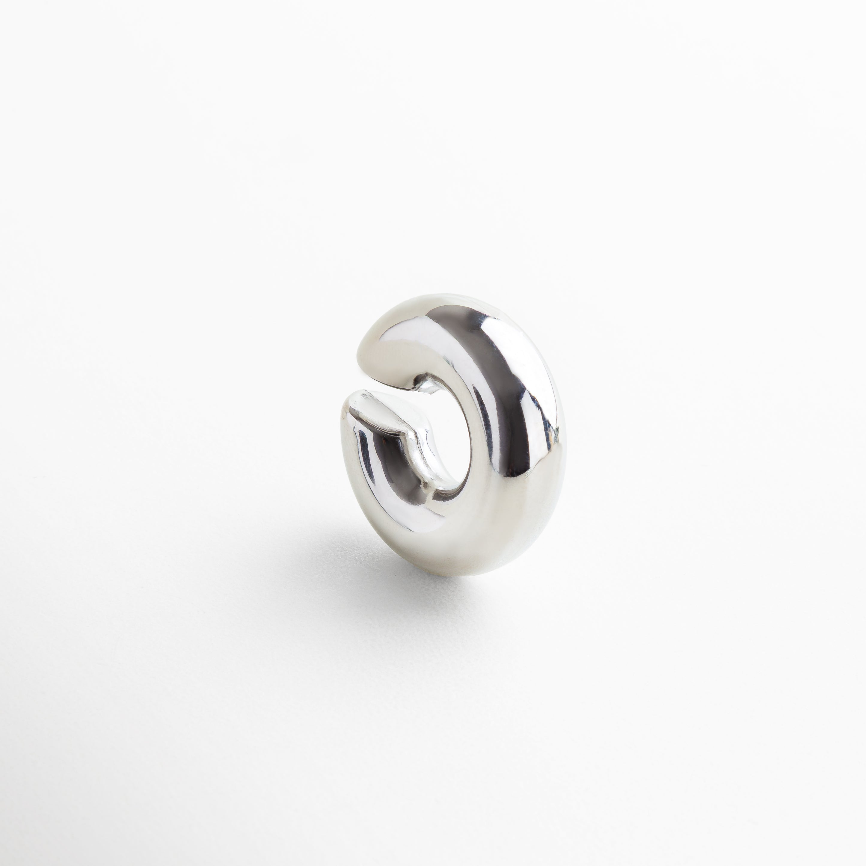 Detalle de ear cuff plateado con acabado brillante y pulido, Primer plano de accesorio para oreja en acero inoxidable, Textura y brillo del ear cuff plateado sin perforación, Diseño contemporáneo en acero inoxidable con baño plateado