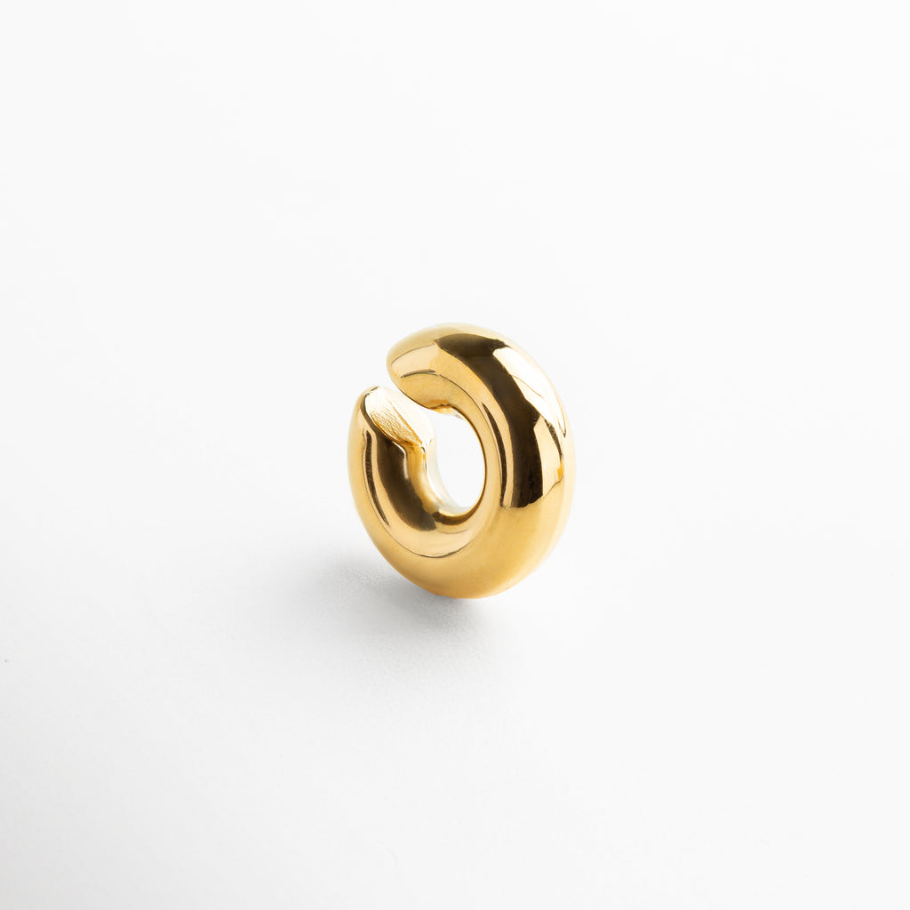 Detalle de ear cuff dorado con acabado pulido y brillante, Primer plano de accesorio para oreja en chapa de oro, Textura y brillo del ear cuff dorado sin perforación, Diseño contemporáneo en acero inoxidable con baño oro 