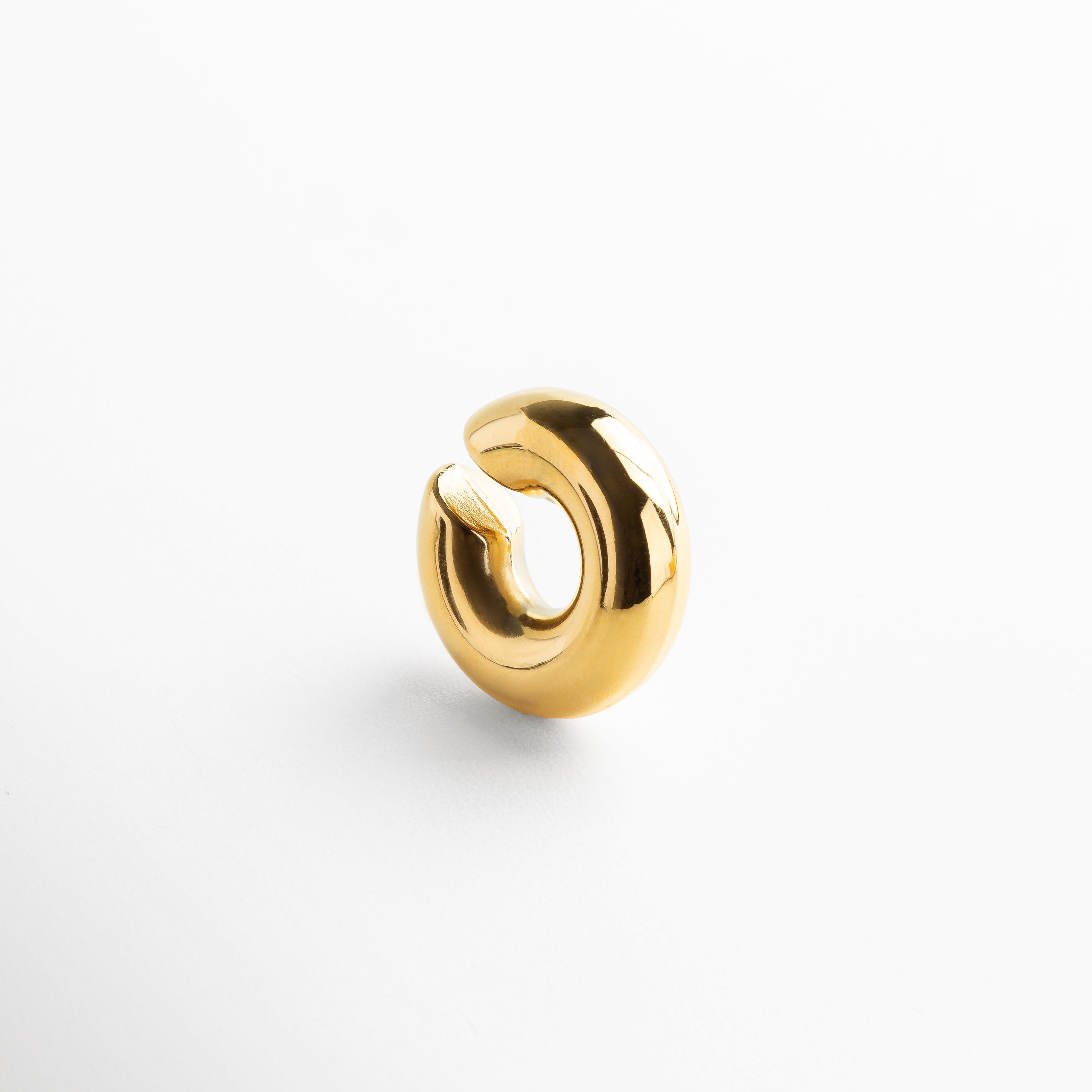 Detalle de ear cuff dorado con acabado pulido y brillante, Primer plano de accesorio para oreja en chapa de oro, Textura y brillo del ear cuff dorado sin perforación, Diseño contemporáneo en acero inoxidable con baño oro 