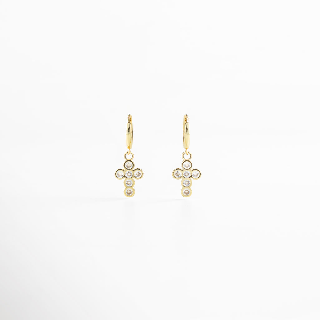Aretes de cruz dorada vistos de frente, con pequeñas zirconias incrustadas que capturan la luz. Vista frontal de los aretes con diseño de cruz brillante, estilo elegante y atemporal. Aretes dorados con zirconias en forma de cruz, fotografía frontal completa sobre fondo neutro. Primer plano frontal de aretes de cruz dorada, destacando su brillo delicado.Par de aretes dorados en forma de cruz con detalles brillantes, vistos de frente.