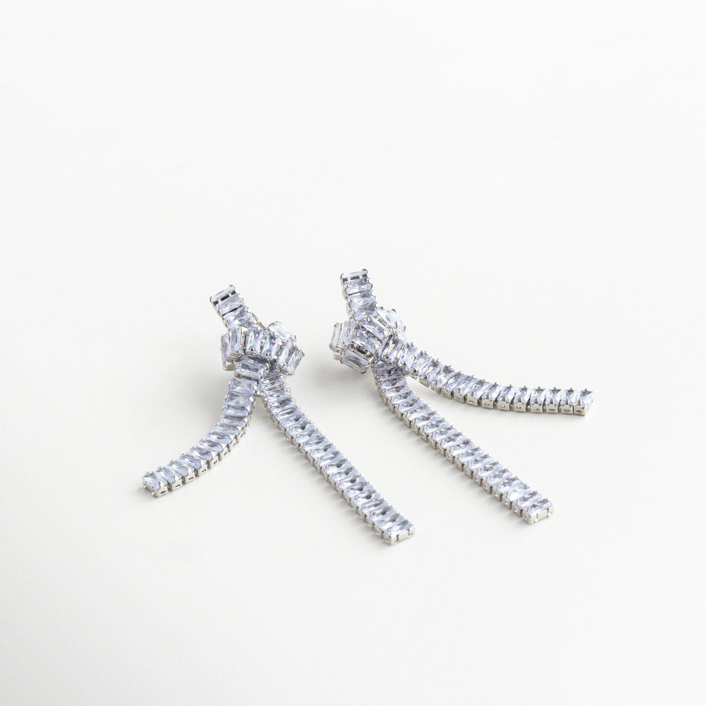 Detalle del nudo plateado con zirconias incrustadas, Primer plano de arete con estructura metálica y gemas, Nudo escultórico en acabado plateado con detalles brillantes, Cadenas decoradas con zirconias en arete plateado


