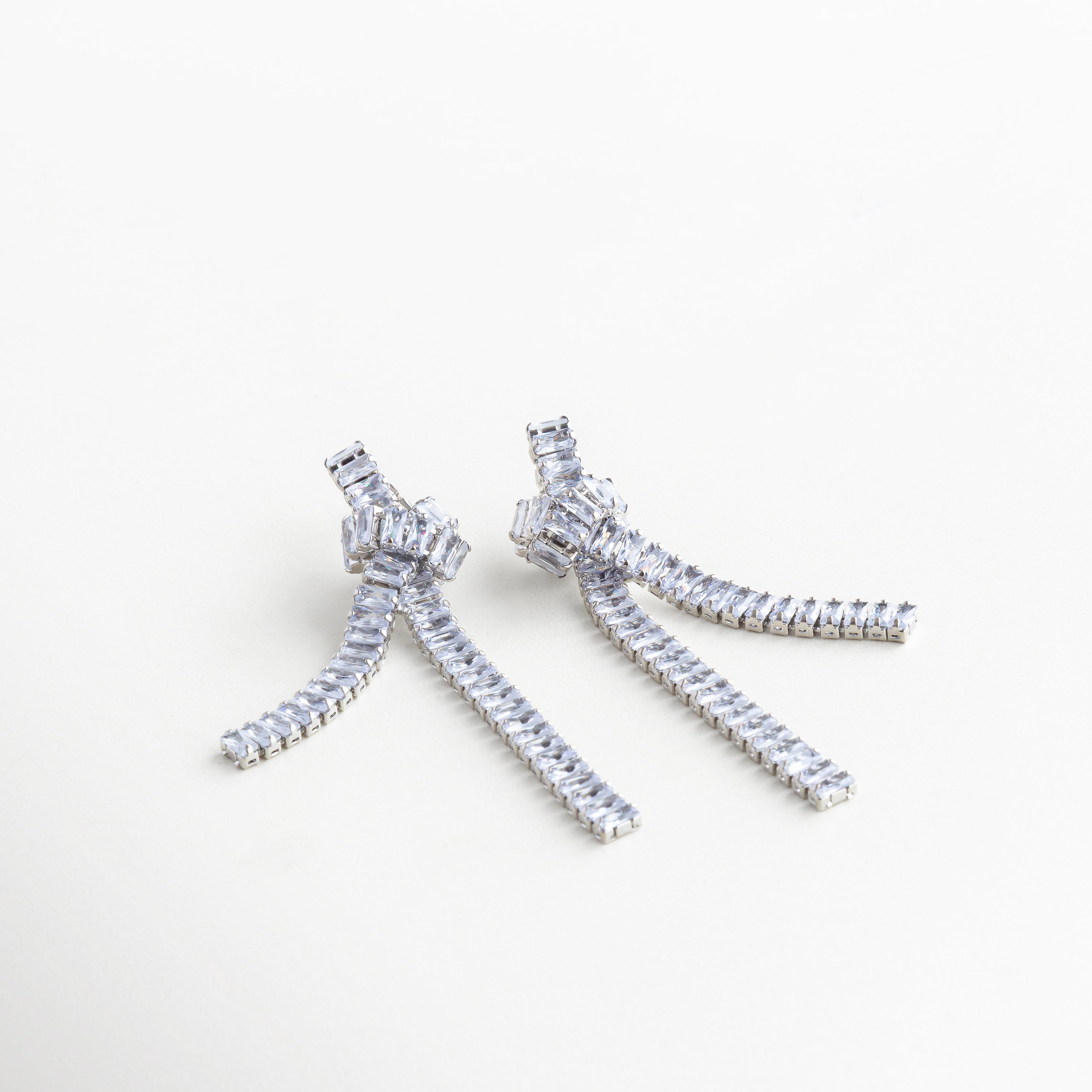 Detalle del nudo plateado con zirconias incrustadas, Primer plano de arete con estructura metálica y gemas, Nudo escultórico en acabado plateado con detalles brillantes, Cadenas decoradas con zirconias en arete plateado

