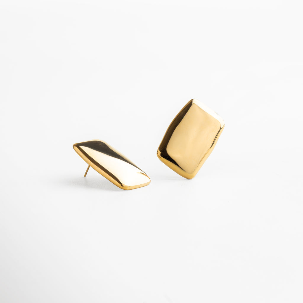 Detalle de aretes con acabado dorado brillante, silueta rectangular y líneas limpias, diseño que combina minimalismo y elegancia, accesorio perfecto para transformar cualquier outfit con sutileza