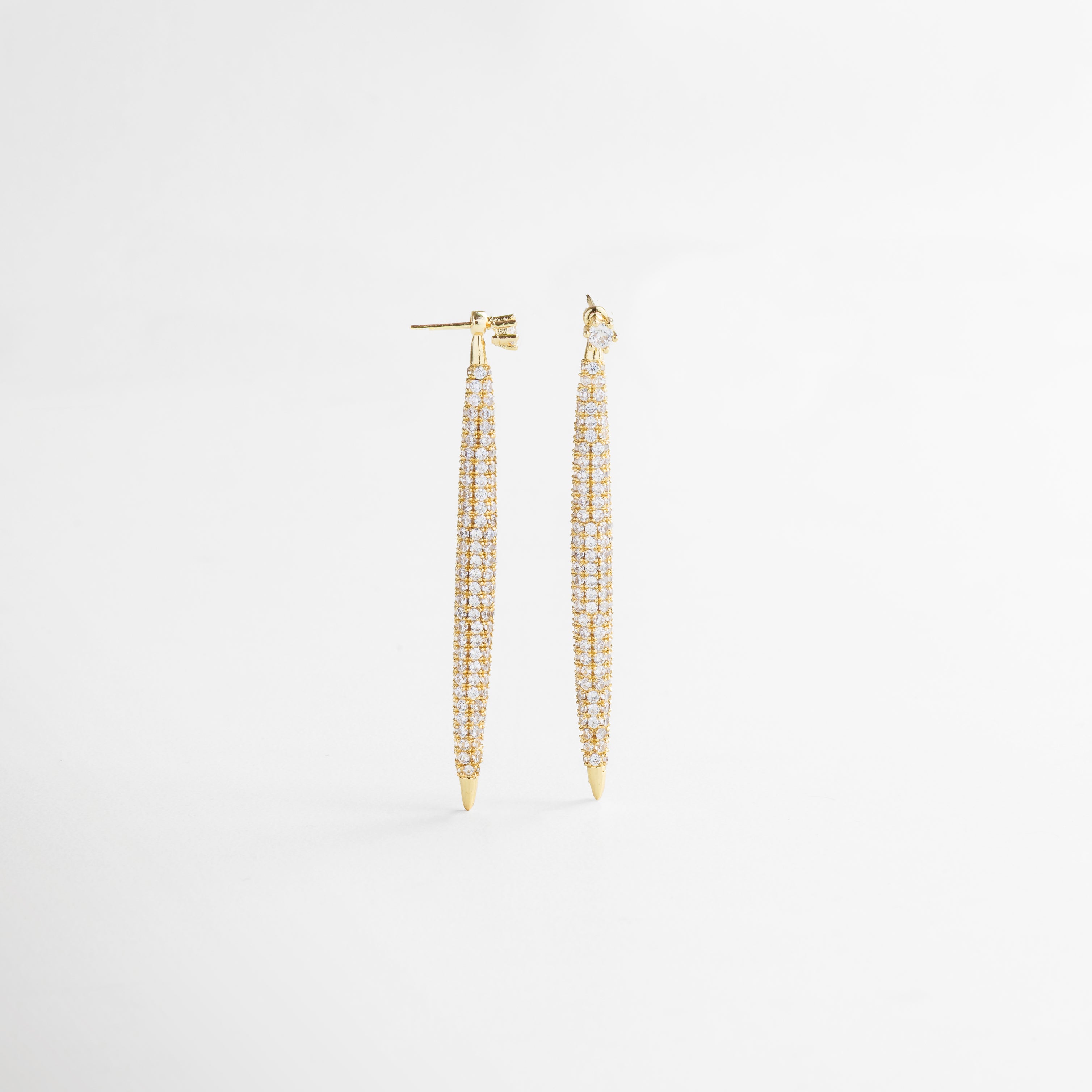 Vista superior de los Aretes Tiznit dorados, mostrando su longitud completa y alineación de zirconias brillantes. Aretes largos en tono dorado vistos desde arriba, con diseño lineal y destellos sutiles.
 Toma cenital de los aretes elegantes con forma alargada y superficie decorada con piedras. Aretes dorados extendidos en vista superior, resaltando su estructura estilizada y acabado brillante. Vista desde arriba de los Aretes Tiznit, con diseño glamuroso y detalles en zirconia sobre chapa de 